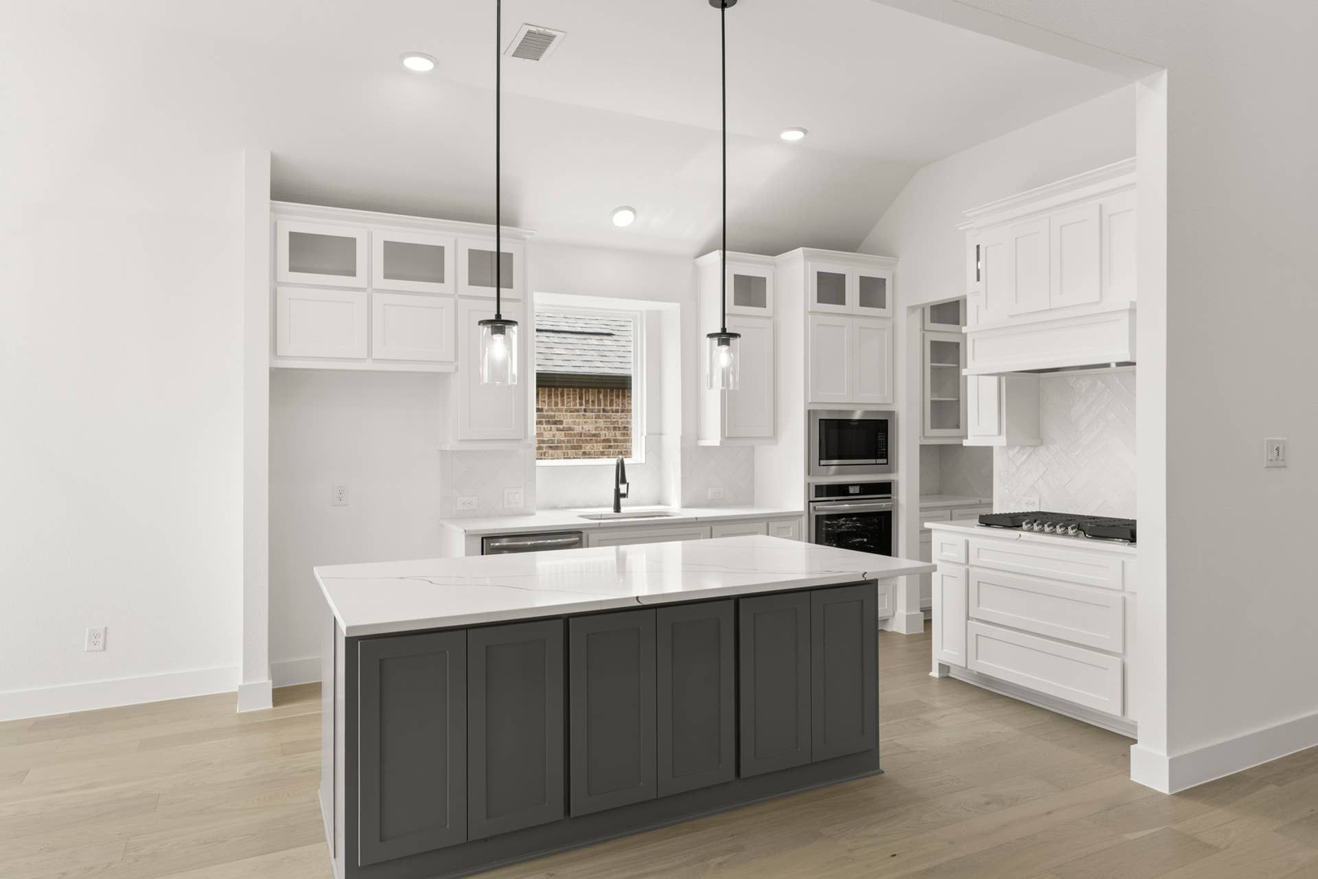 Modern kitchen with white cabinetry, dark island, and pendant lighting.