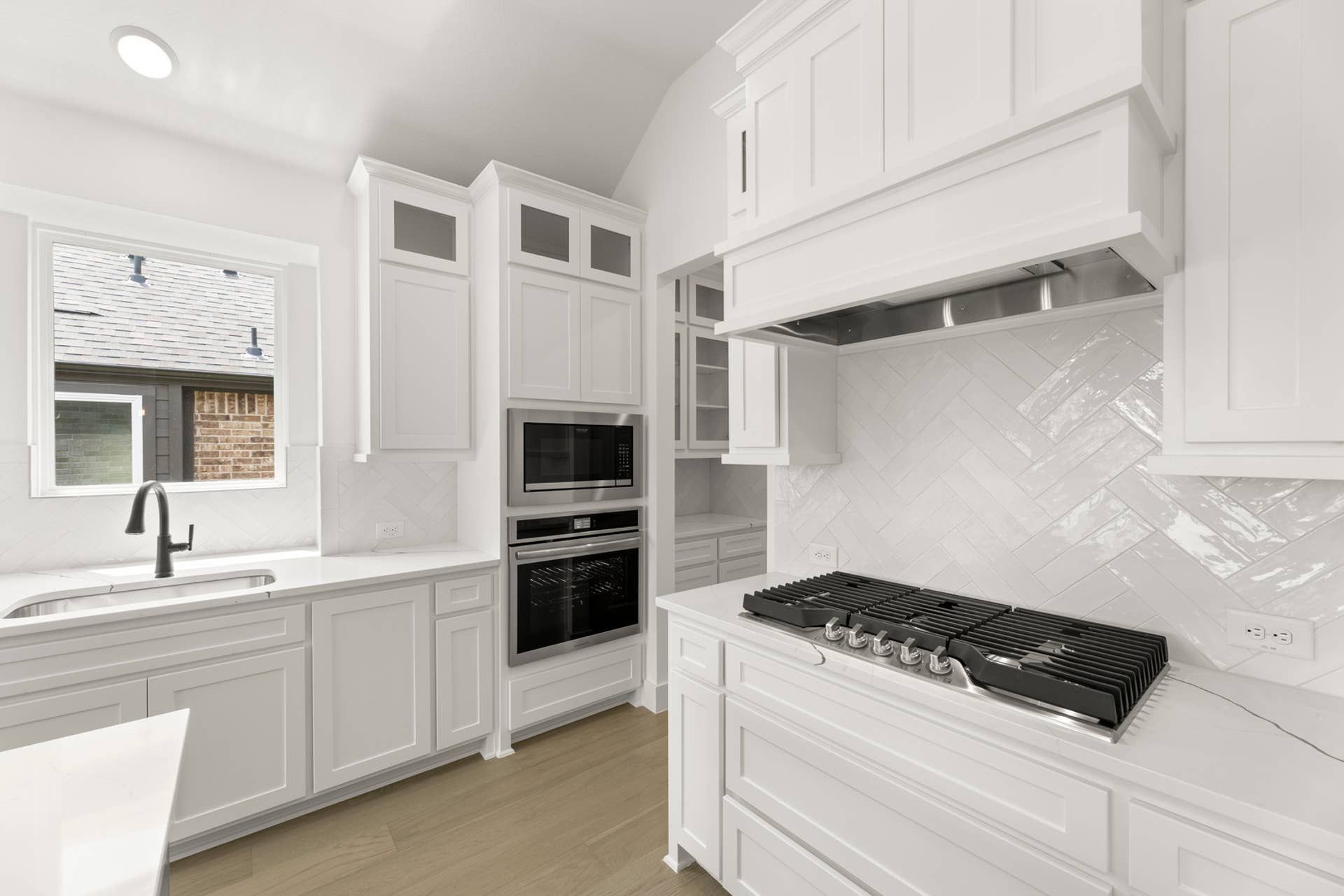 Modern white kitchen with sleek cabinetry, herringbone backsplash, and stainless steel appliances.