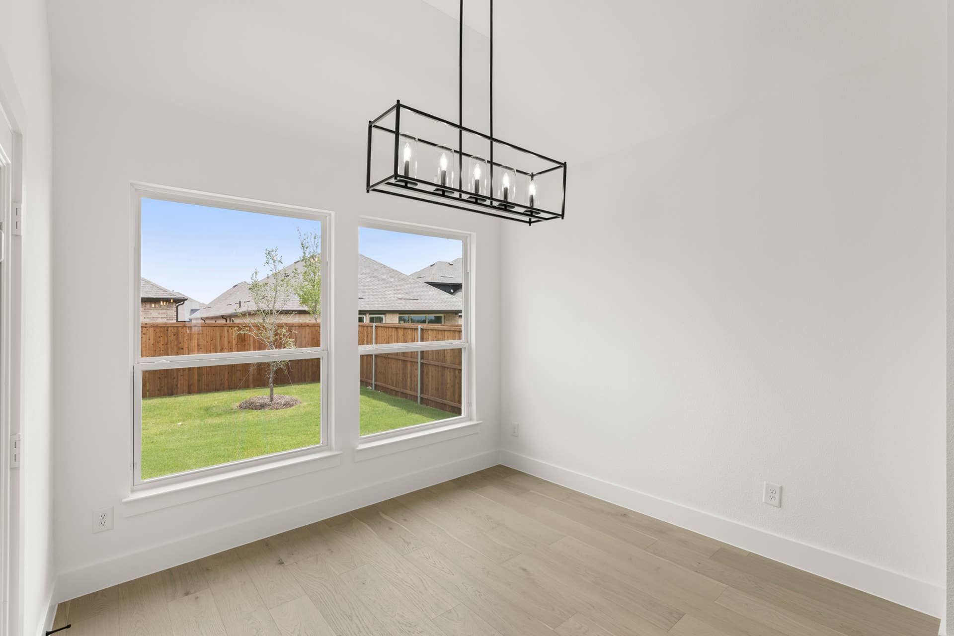 Bright dining nook with modern chandelier and large windows overlooking backyard.