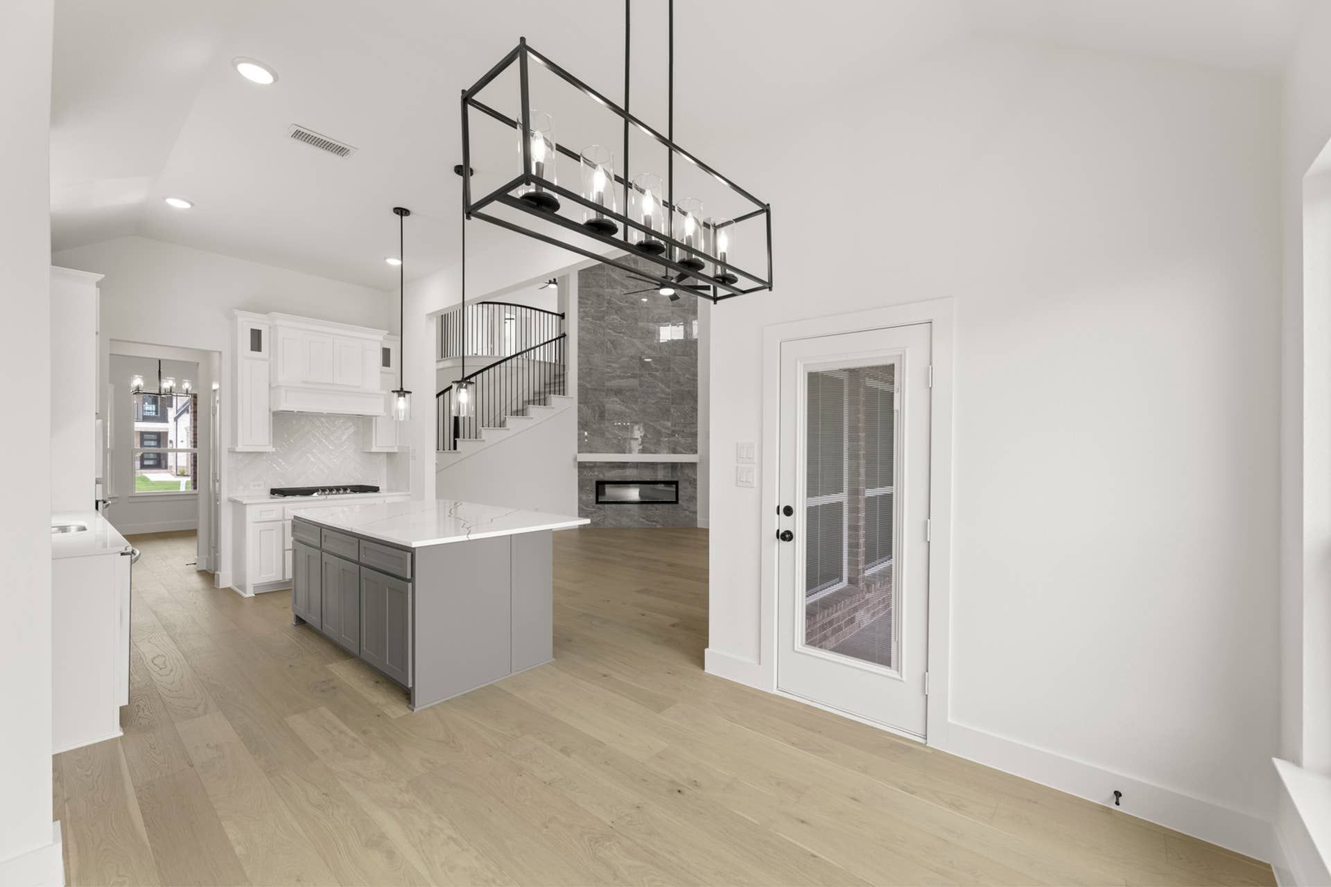 Modern kitchen interior with island, pendant lighting, and open staircase view.