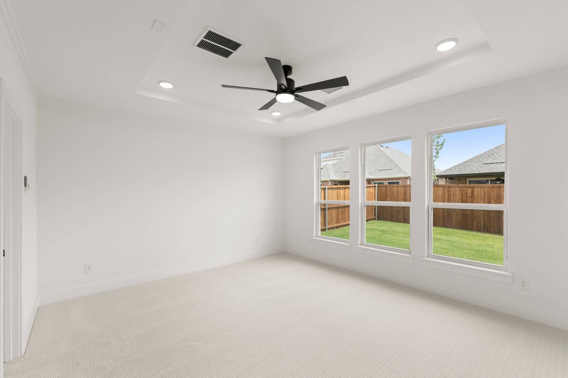 Spacious white room with ceiling fan and large windows overlooking backyard.