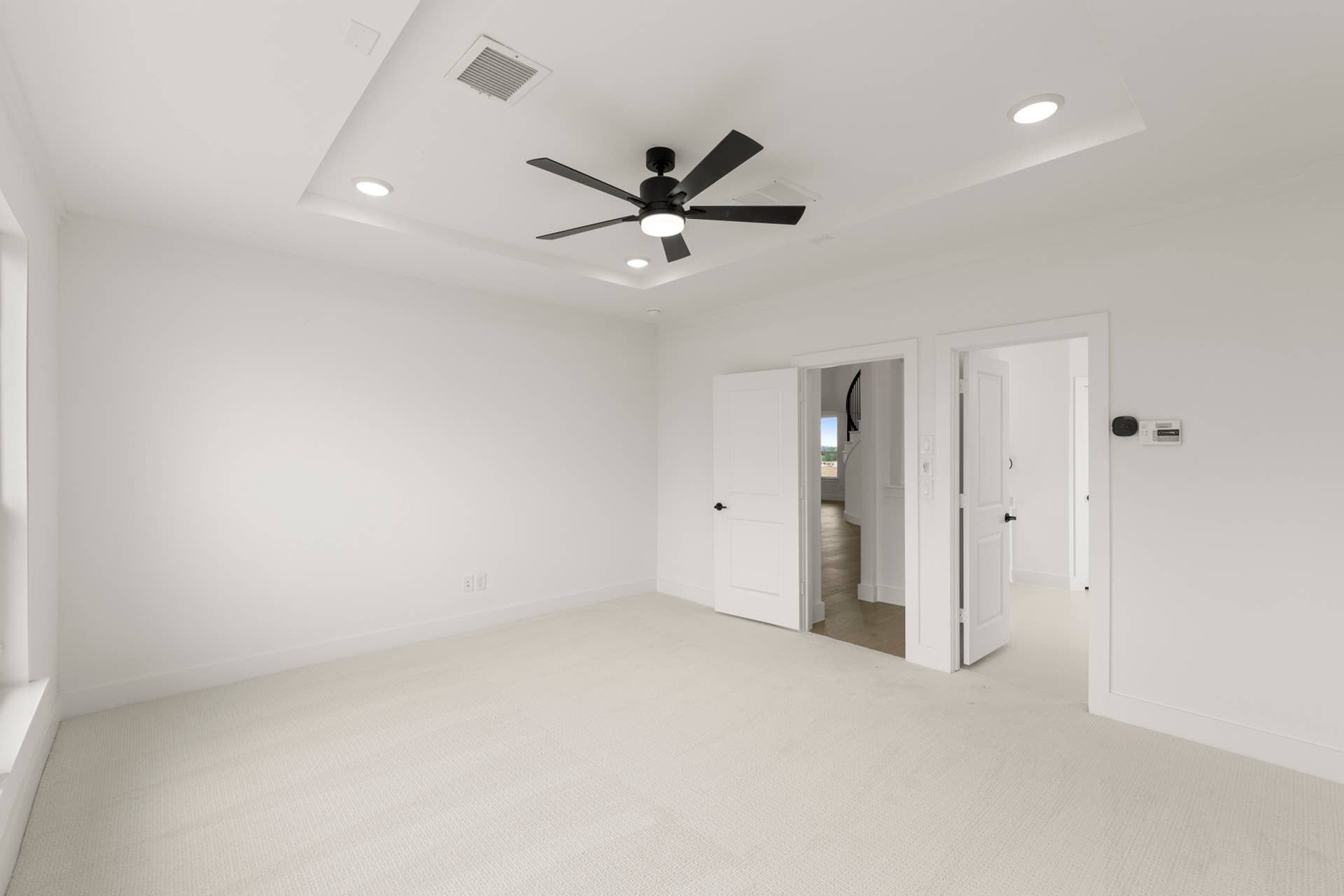 Spacious bedroom with tray ceiling, modern fan, and light neutral carpet.