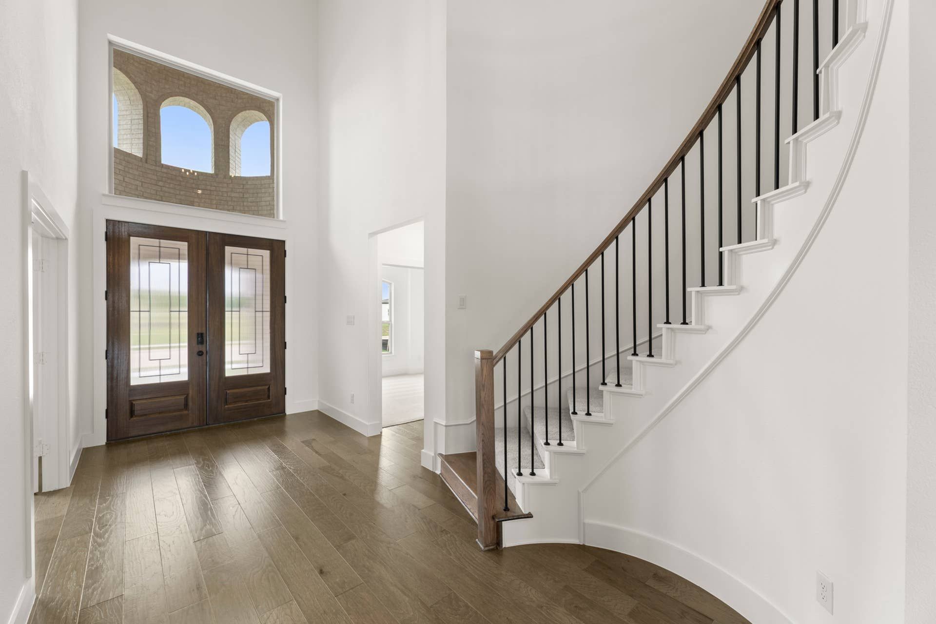 Spacious entryway with curved staircase and wooden double doors.
