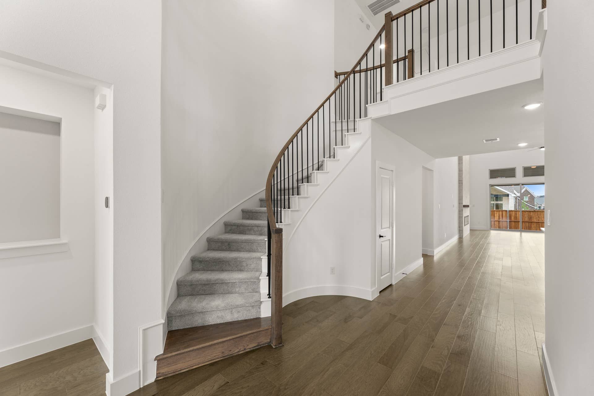 Elegant curved staircase with wooden railing in a bright, modern entryway.