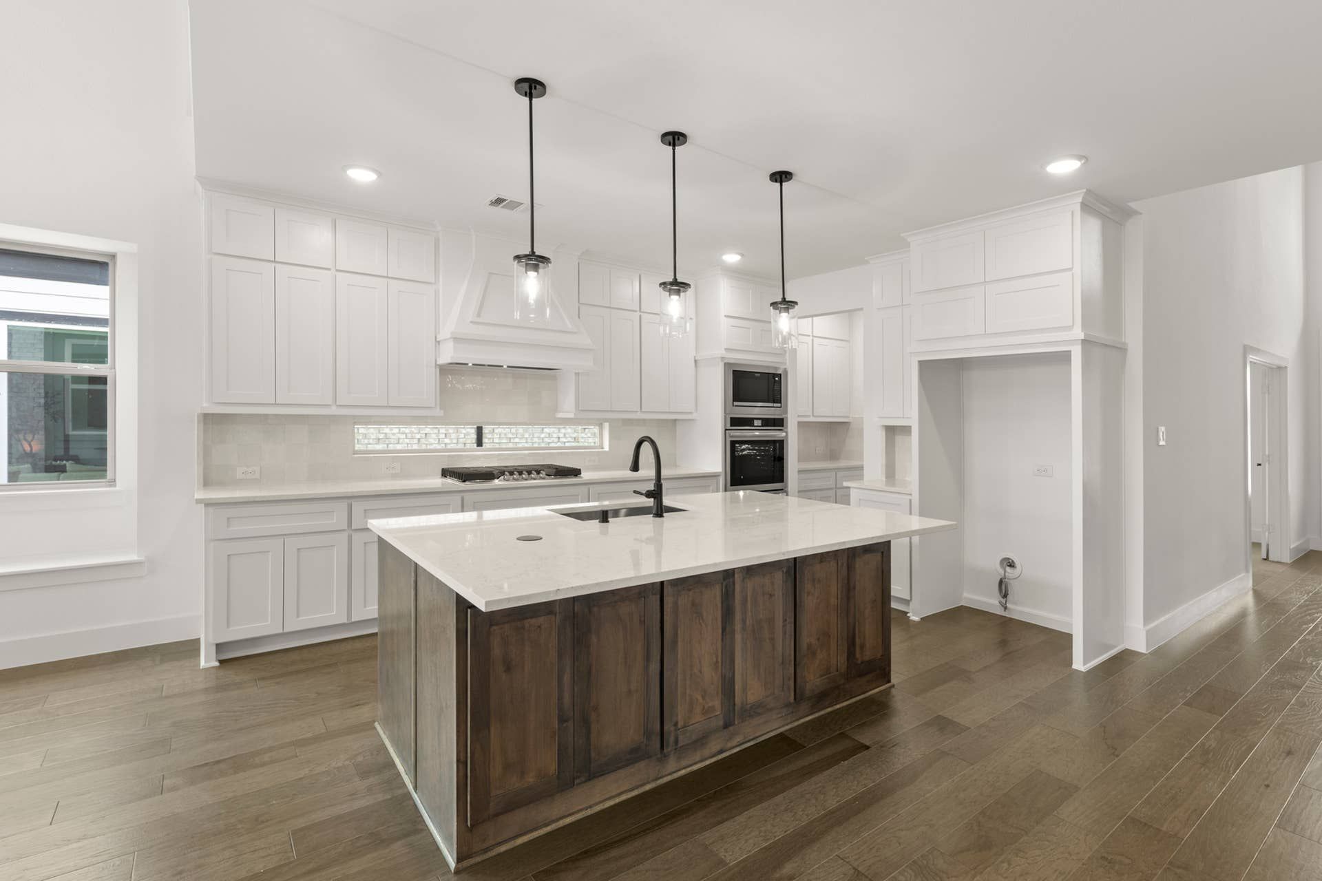 Modern kitchen with white cabinetry, island, pendant lights, and hardwood floors.