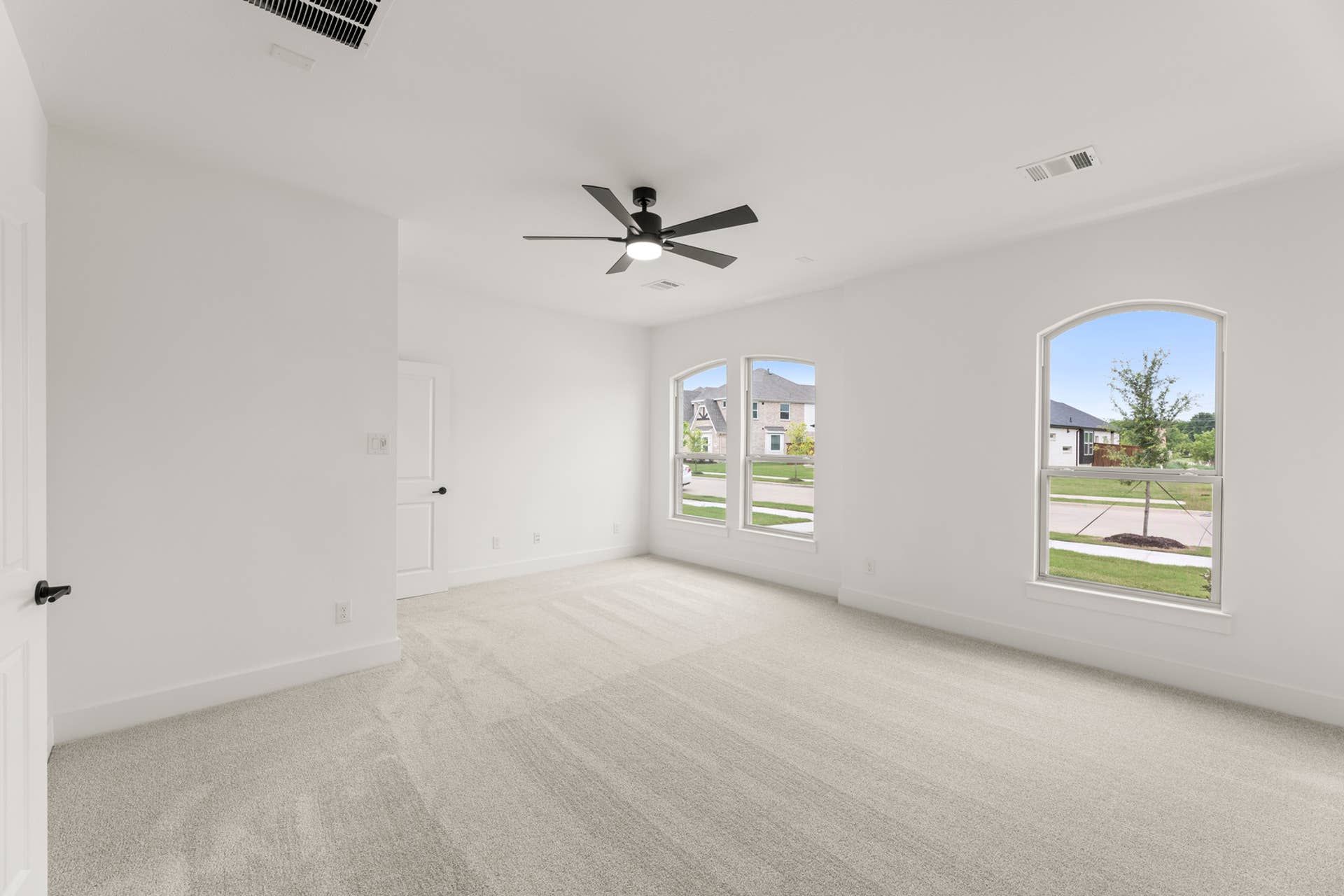 Bright, spacious room with carpet flooring and large windows overlooking neighborhood.
