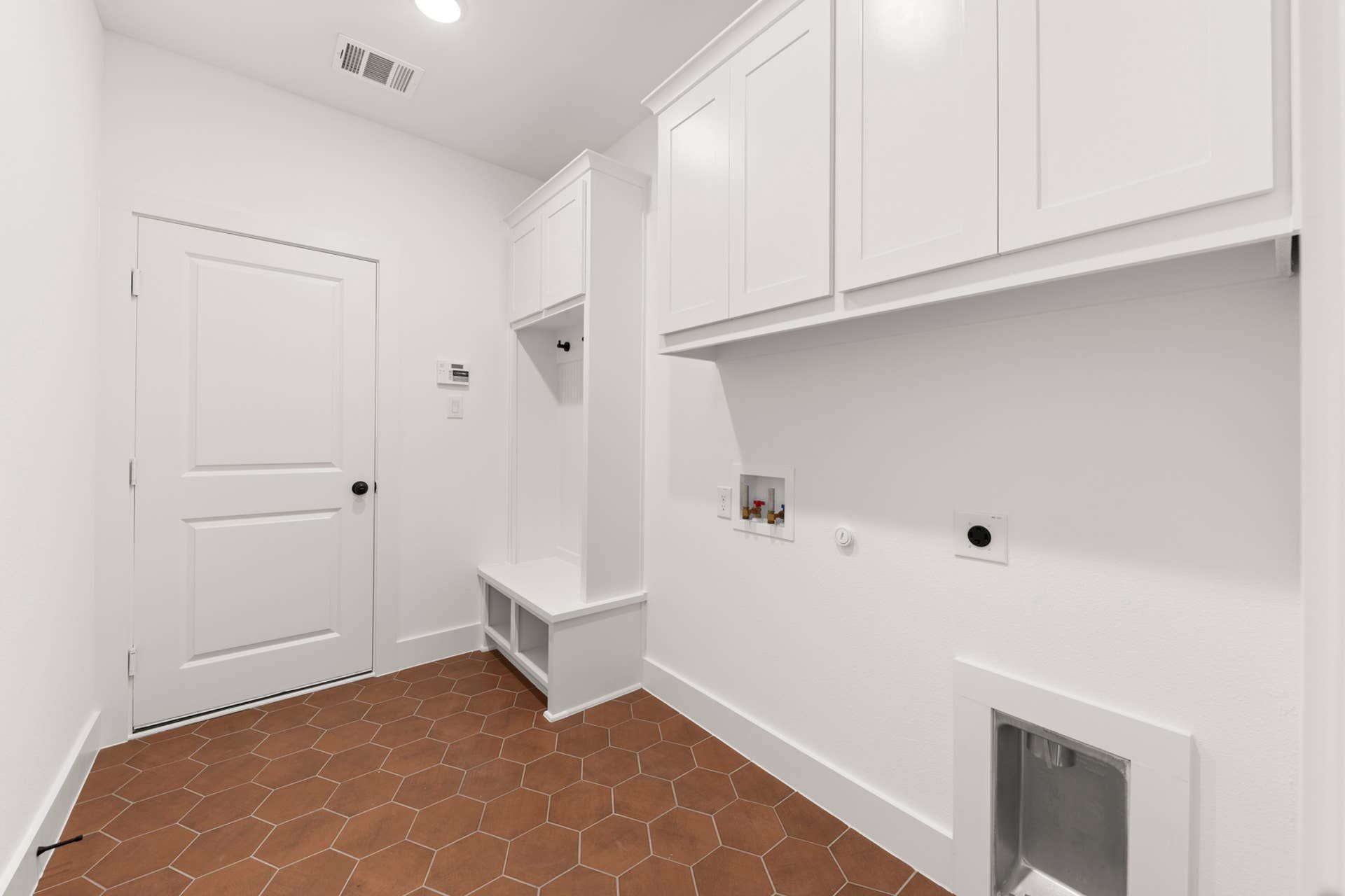 Utility room with white cabinets and hexagonal terracotta floor tiles.