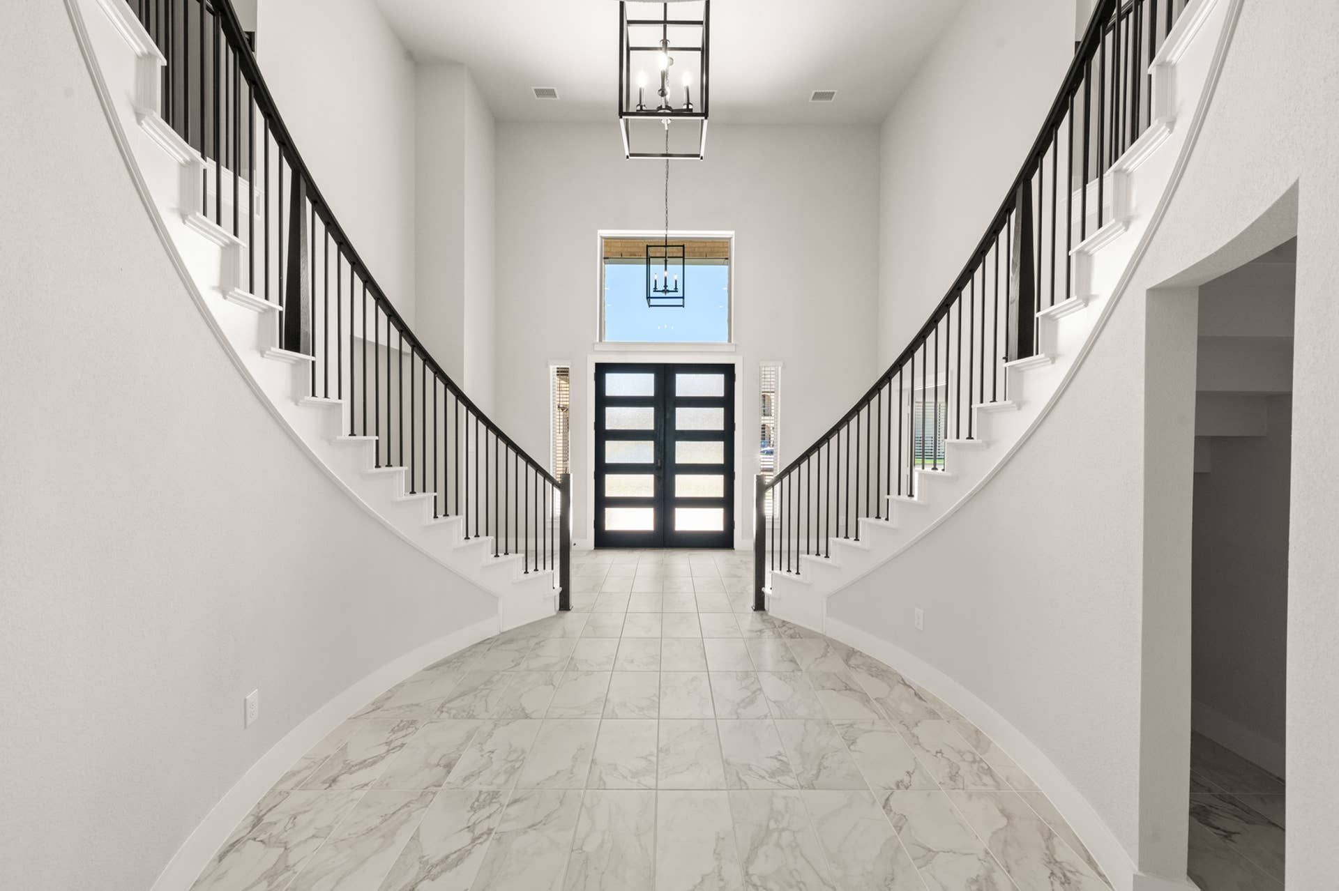 Elegant entryway with dual curved staircases and modern chandelier in luxurious home.