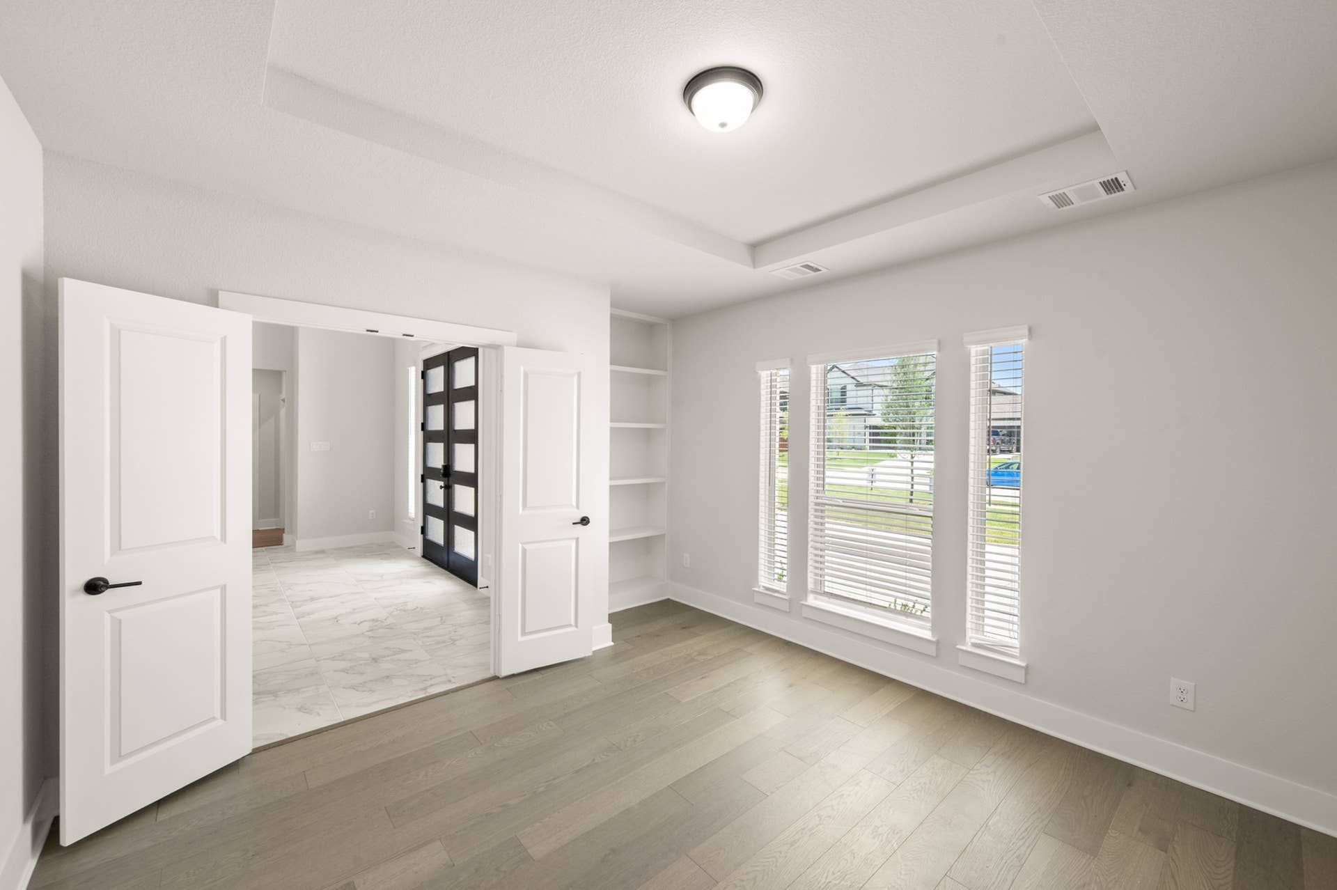 Bright study room with wood floors, large windows, and double doors.