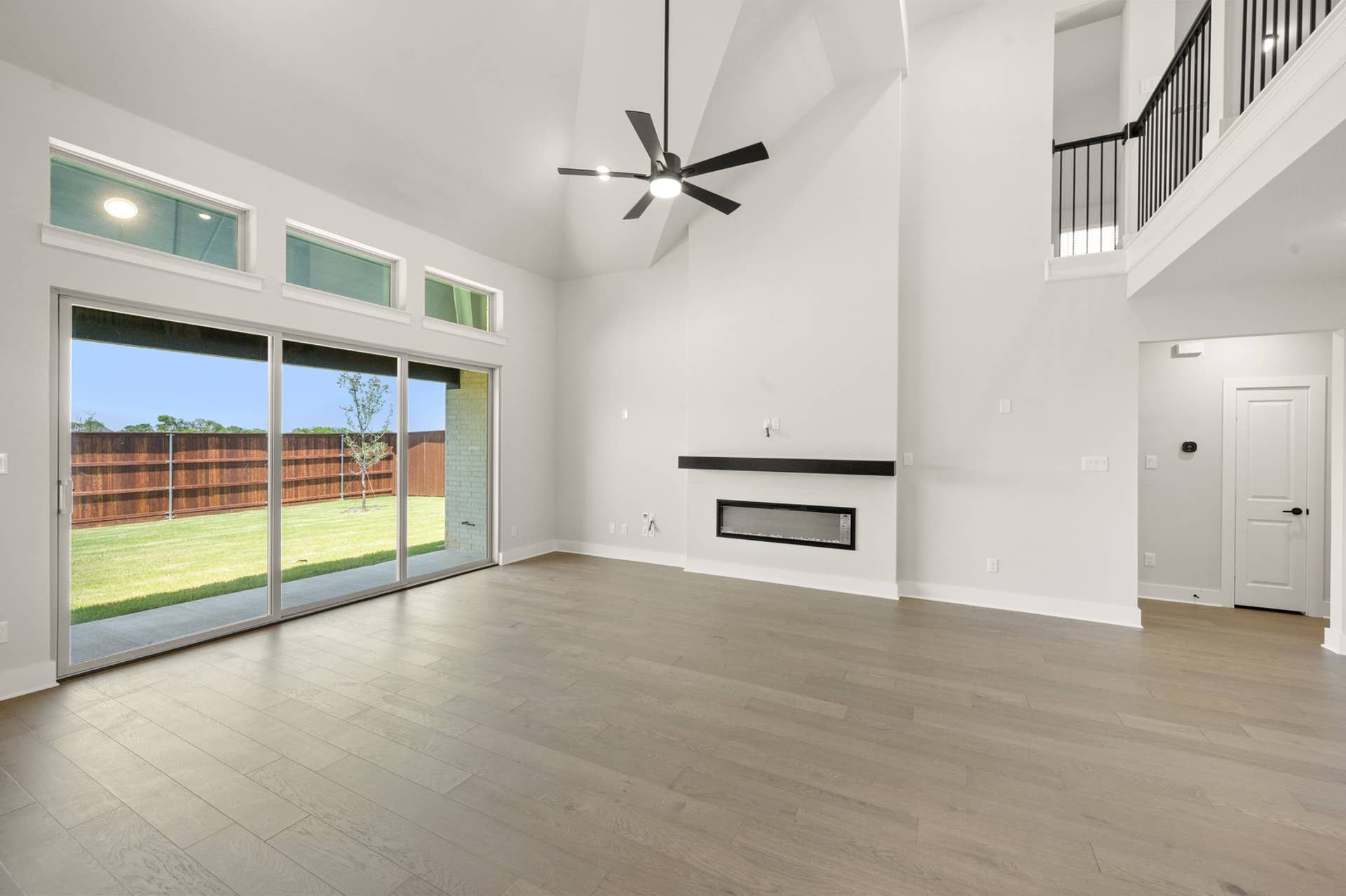 Spacious living room with high ceiling, modern fireplace, and large sliding glass doors.