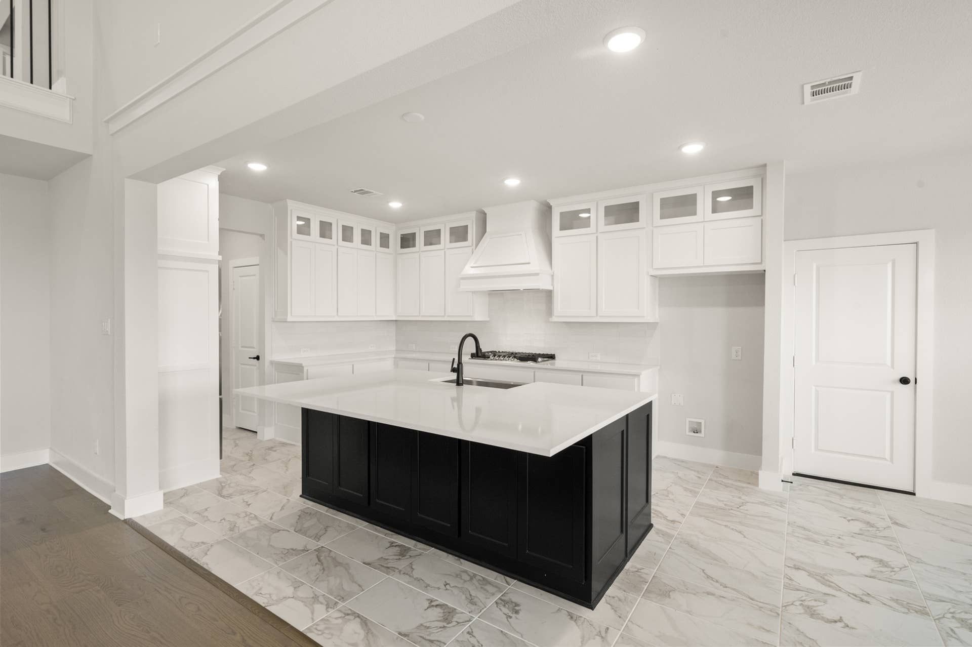 Modern kitchen with white cabinetry, black island, and marble flooring.