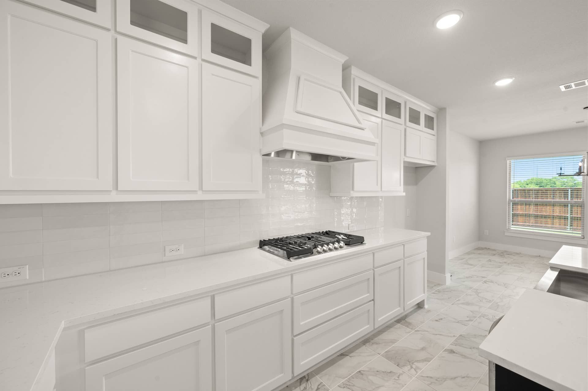 Modern kitchen with white cabinetry, gas cooktop, and marble tile flooring.