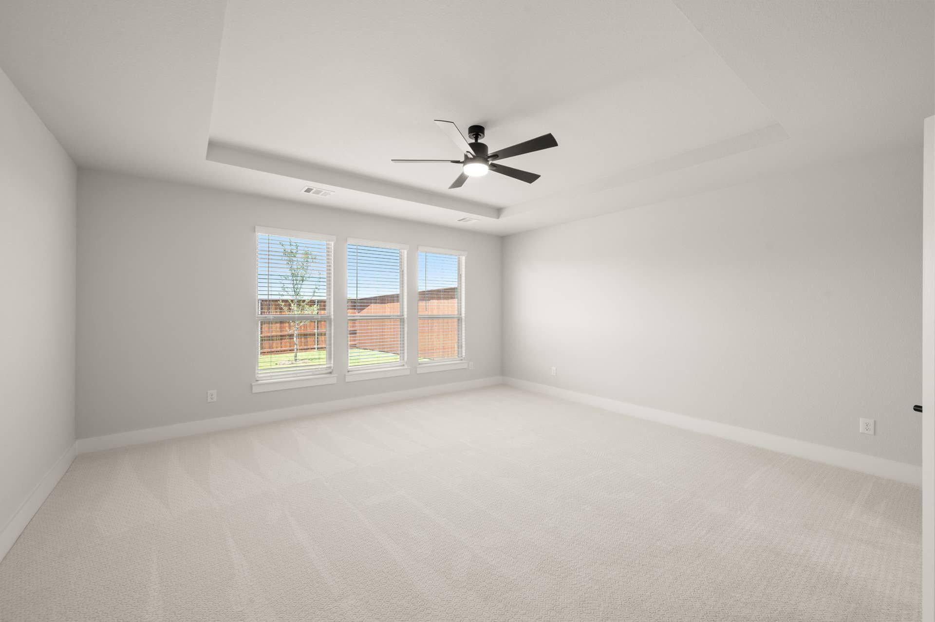 Spacious primary suite with large windows and ceiling fan, carpeted floor.