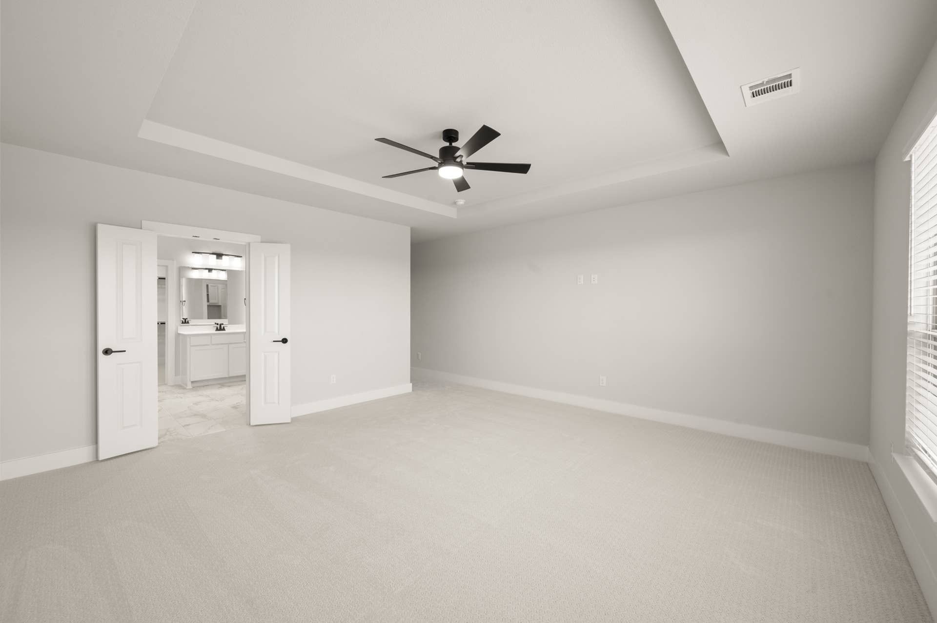 Spacious primary suite with tray ceiling and ceiling fan, leading to modern ensuite bathroom.