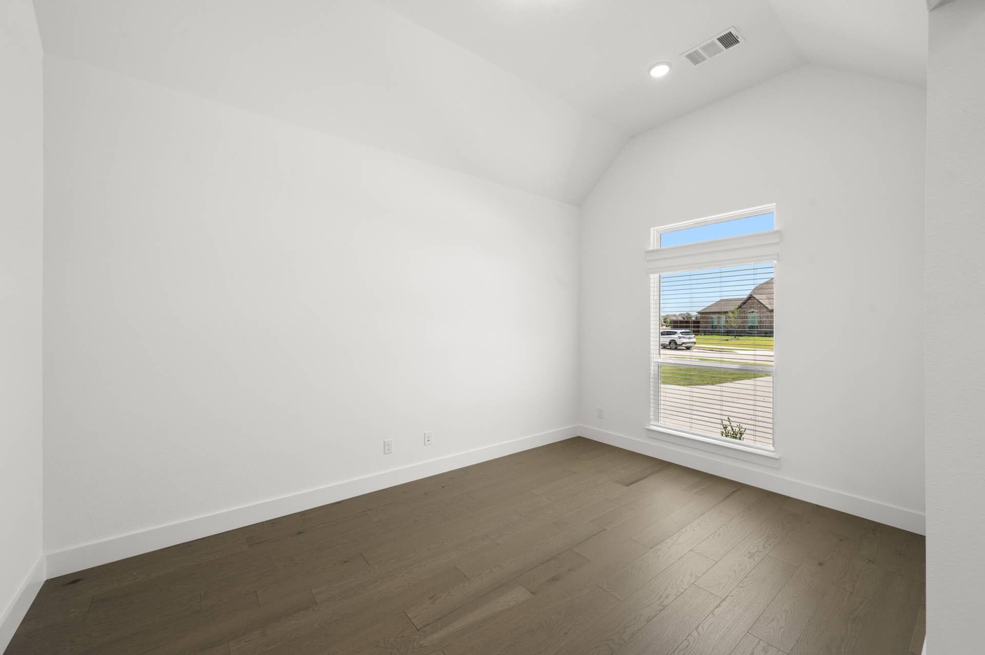 Bright, empty room with vaulted ceiling and large window overlooking street view.