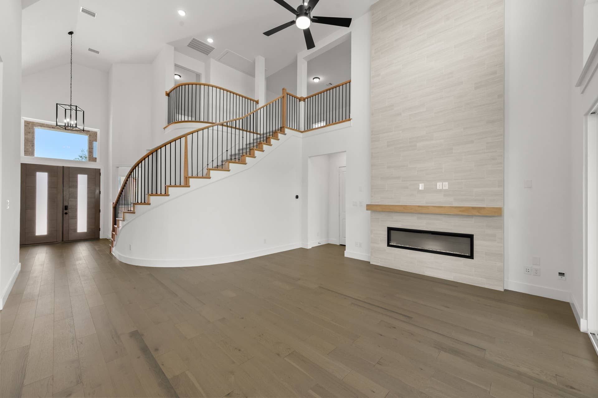 Spacious living room with curved staircase, modern fireplace, and high ceiling fan.