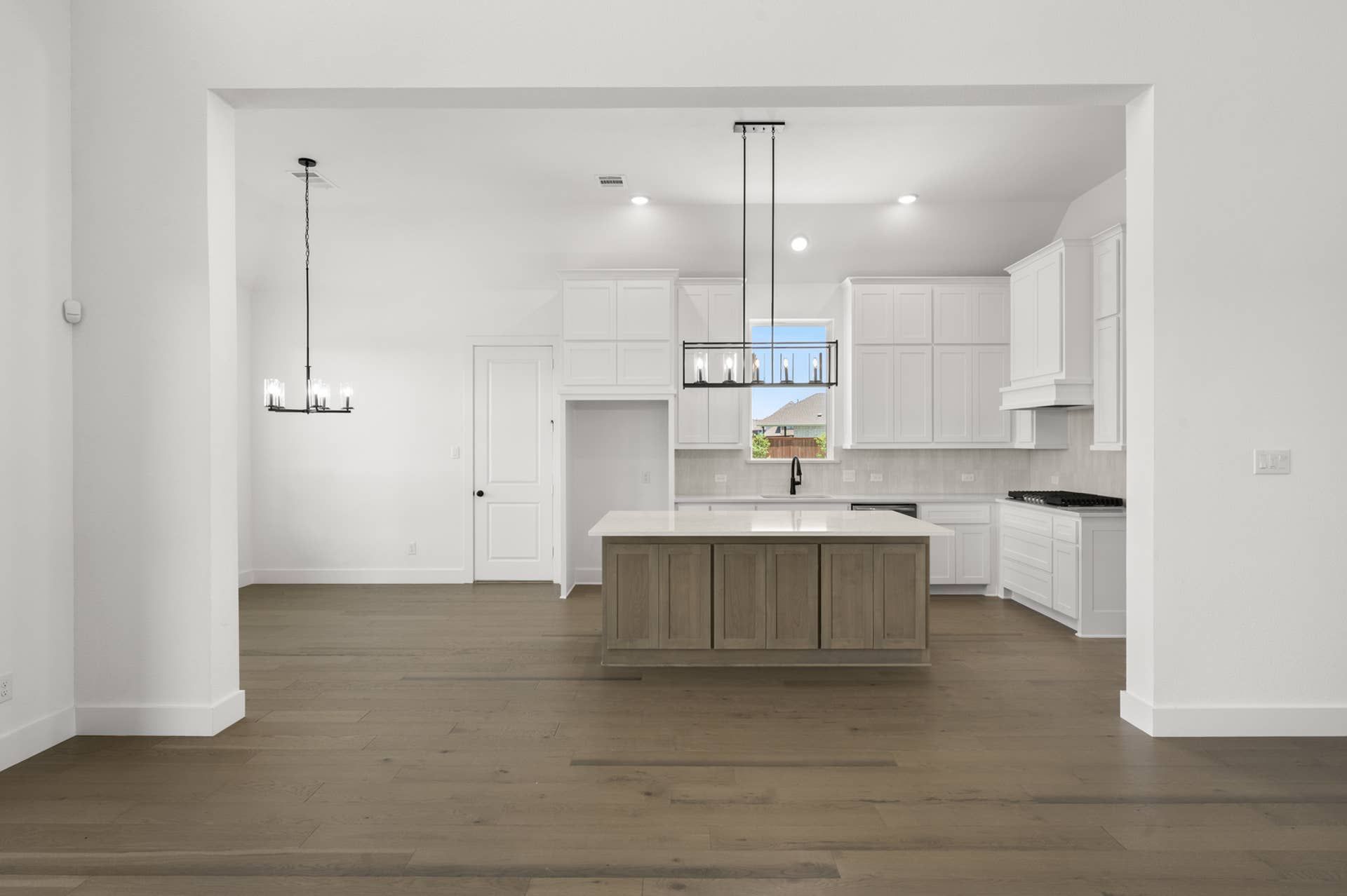 Spacious modern kitchen with island, white cabinetry, and hardwood floors.