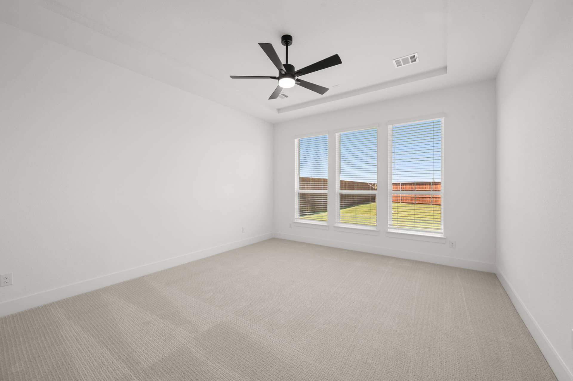 Spacious primary suite with large windows and ceiling fan.