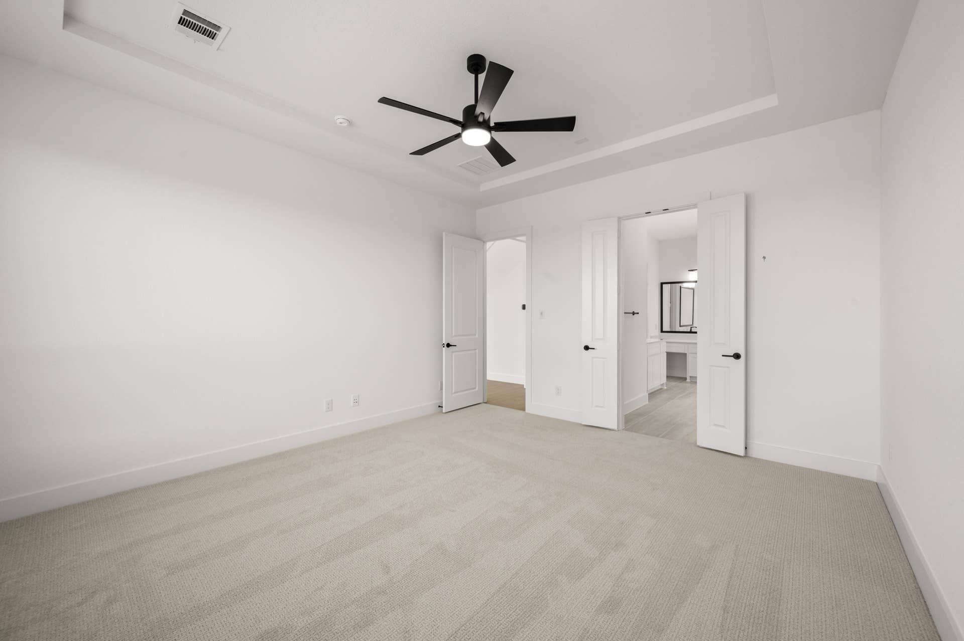 Spacious primary suite with carpeted floor and modern ceiling fan.
