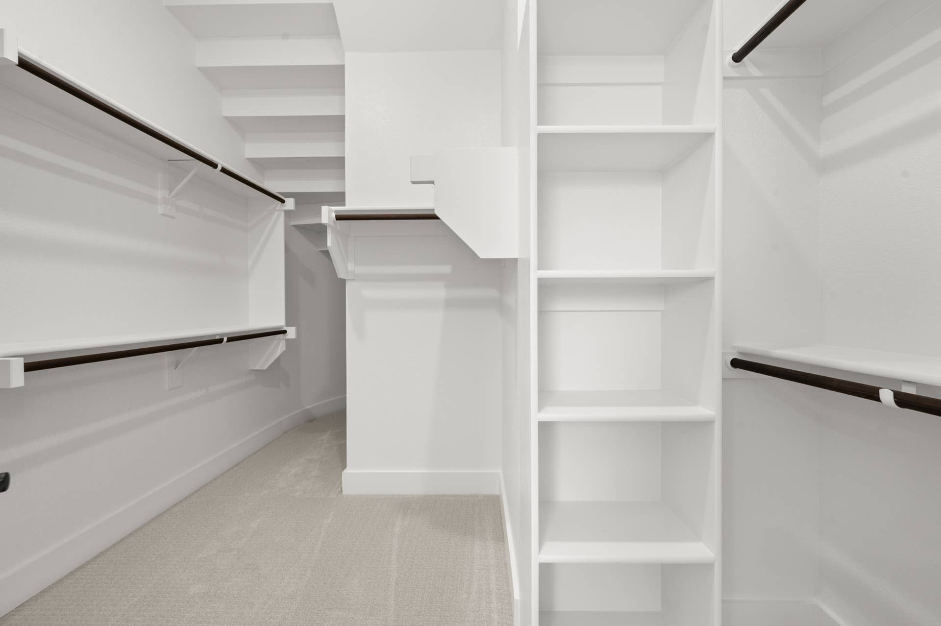 Spacious walk-in closet with white shelving and dark wood rods.