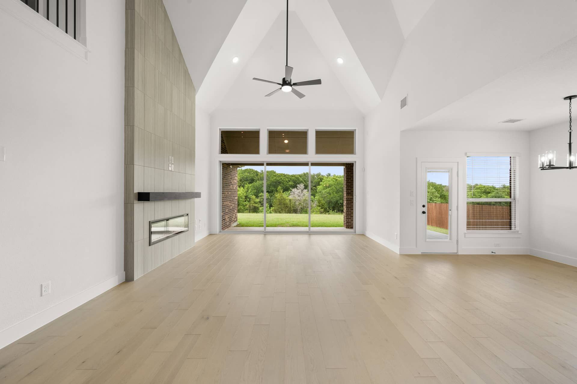 Spacious living room with vaulted ceiling, modern fireplace, and large windows overlooking greenery.