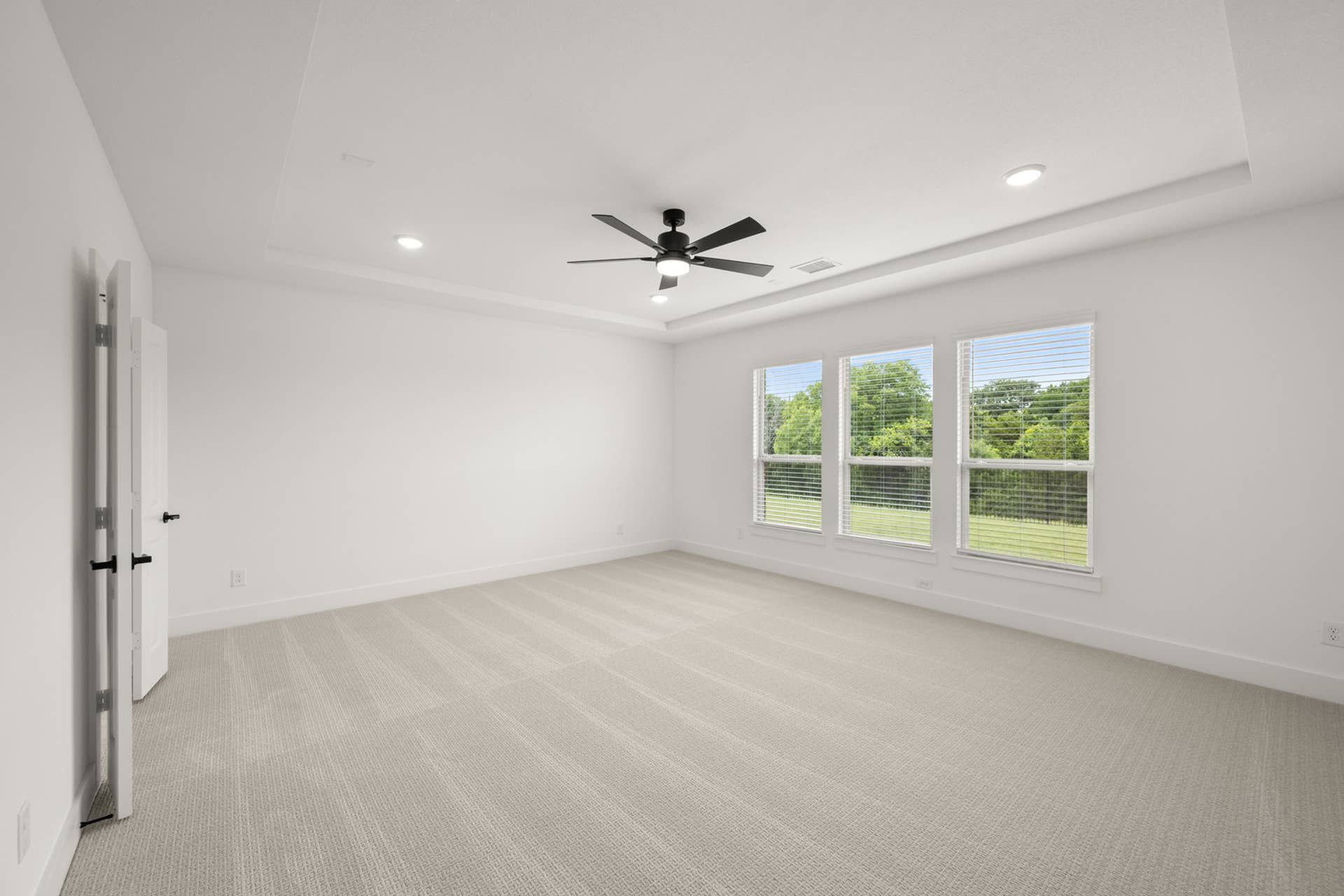 Spacious primary suite with large windows and ceiling fan.