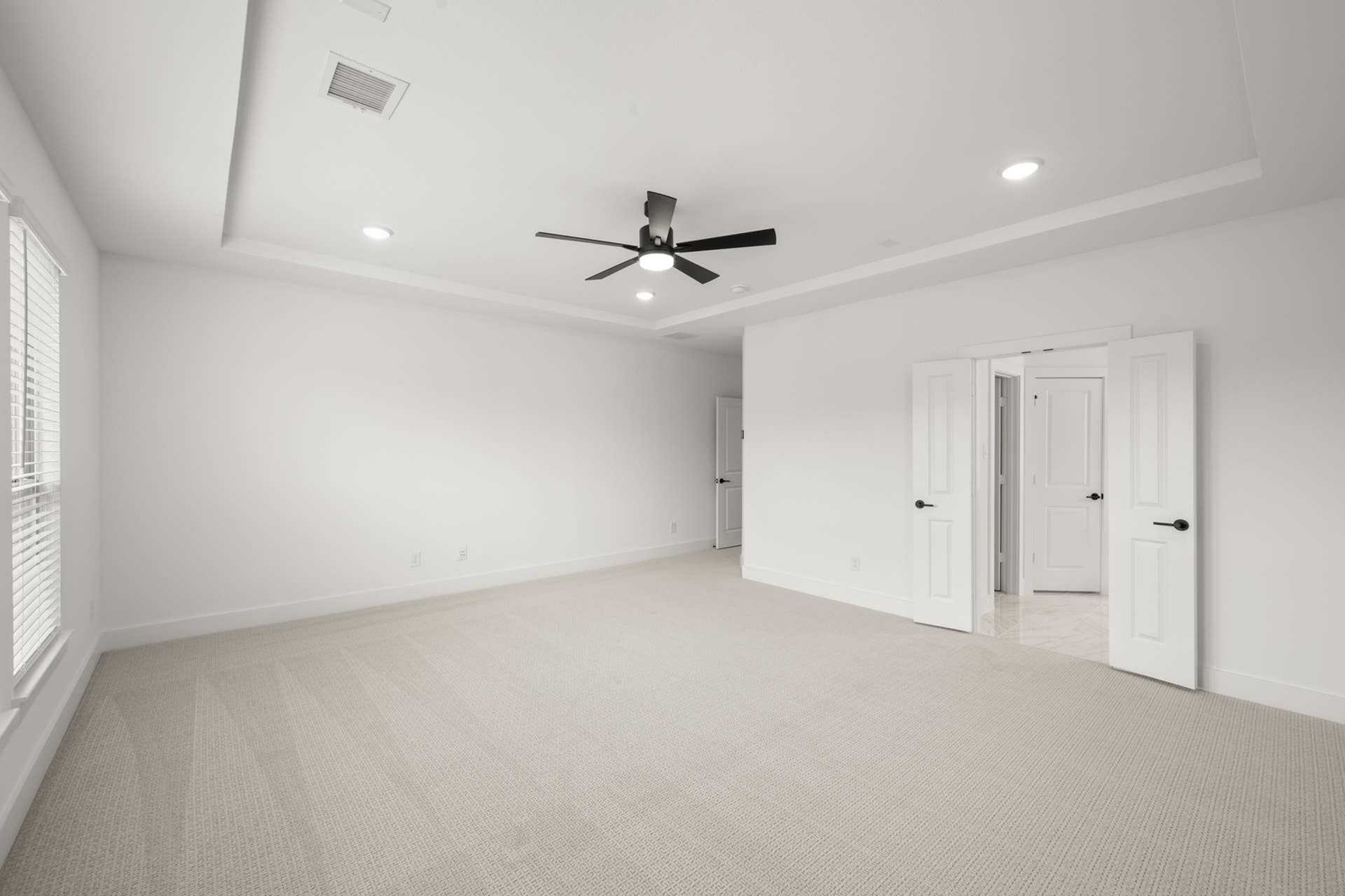 Spacious primary suite with ceiling fan and open double doors.