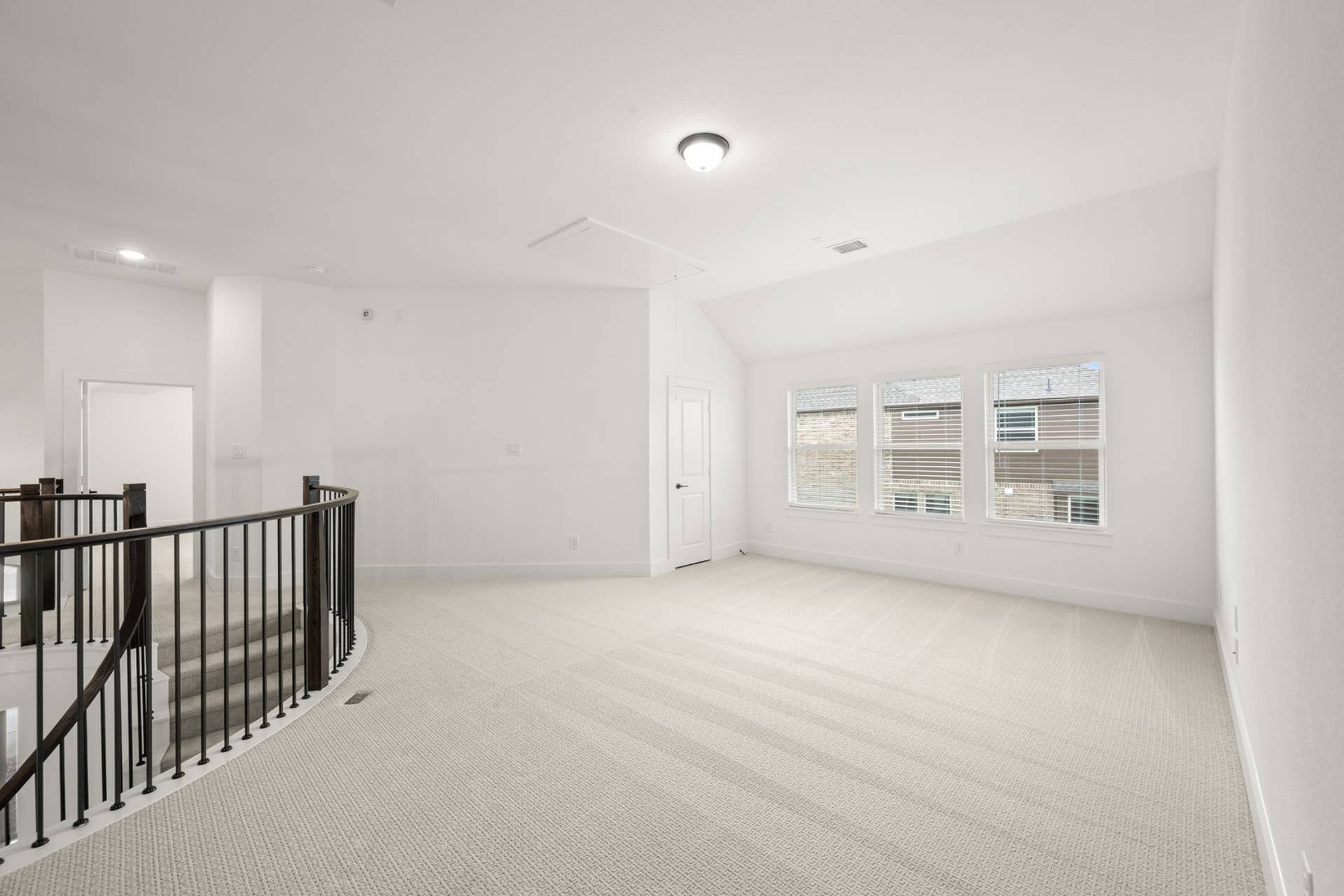 Spacious, carpeted game room with natural light and curved staircase railing.