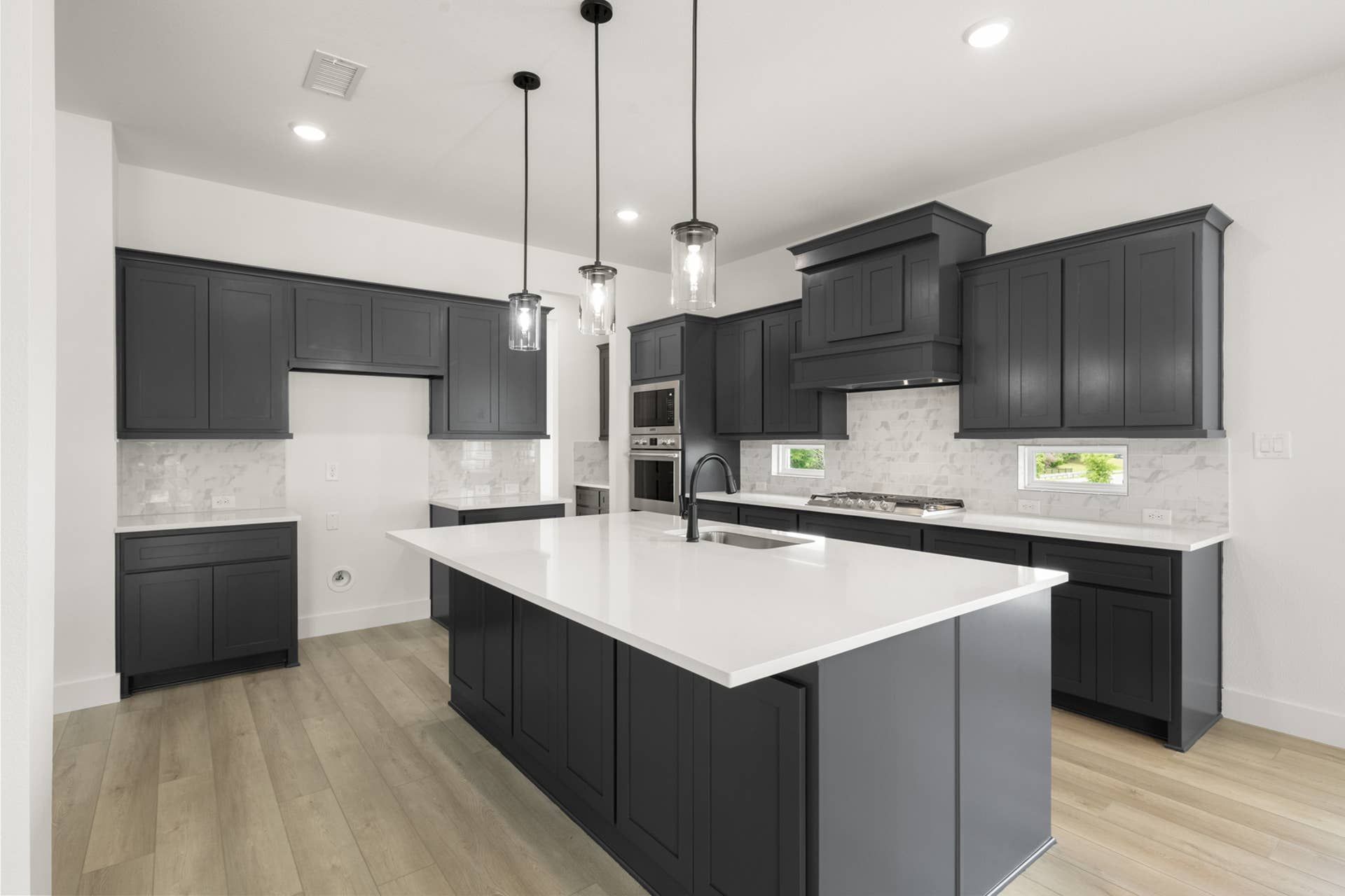 Modern kitchen with dark cabinets, white countertops, and island with pendant lighting.