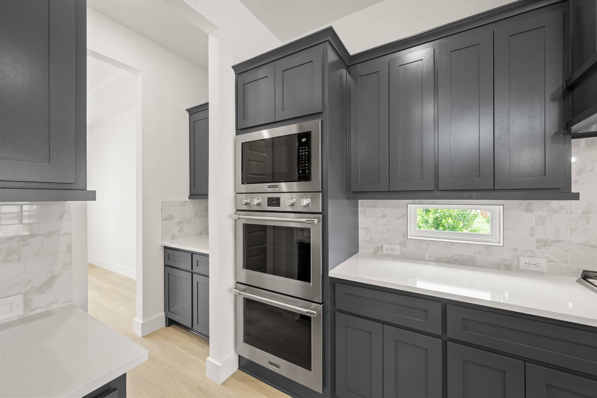 Modern kitchen with dark cabinets, stainless steel appliances, and white countertops.