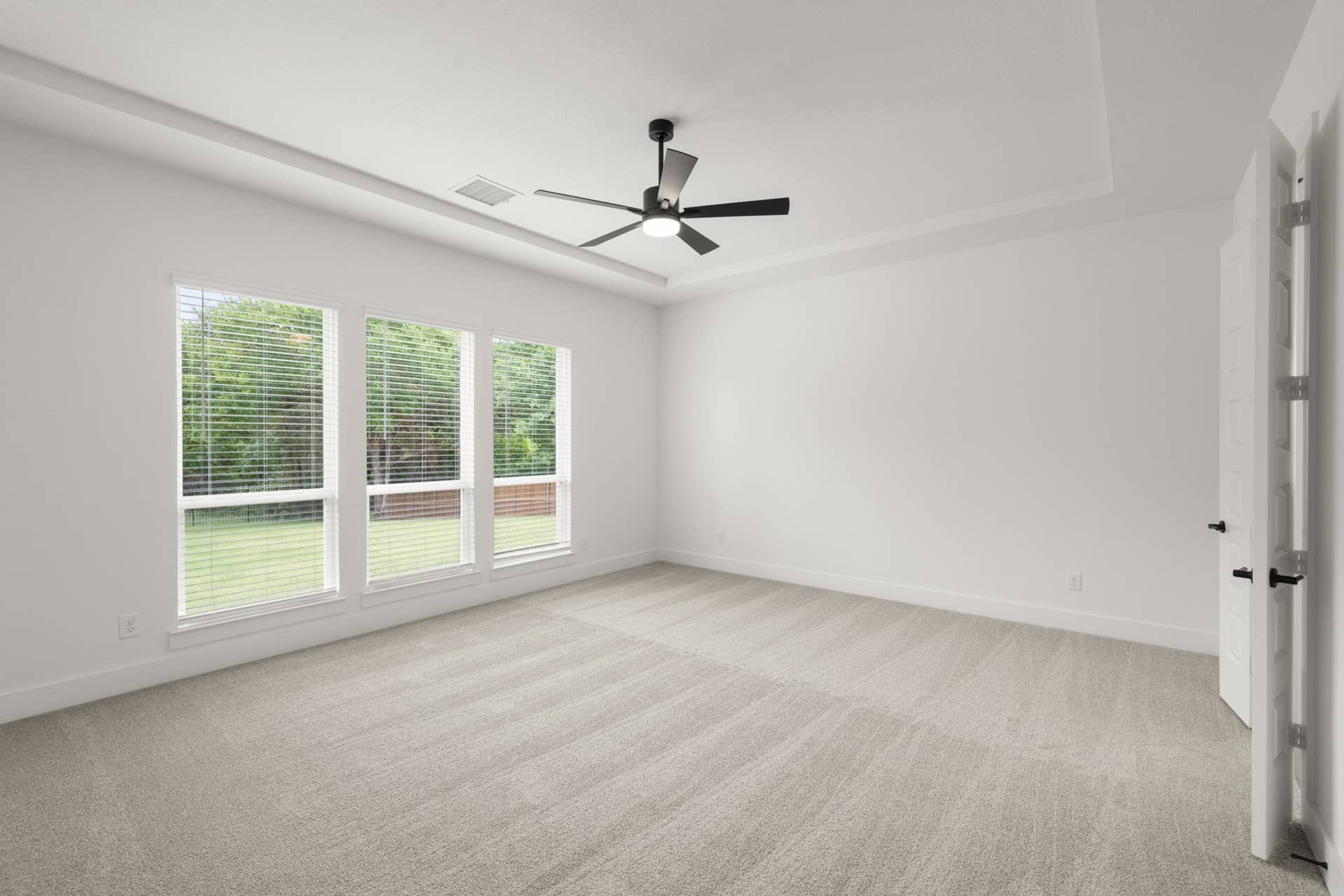 Spacious primary suite with large windows, carpet flooring, and ceiling fan.