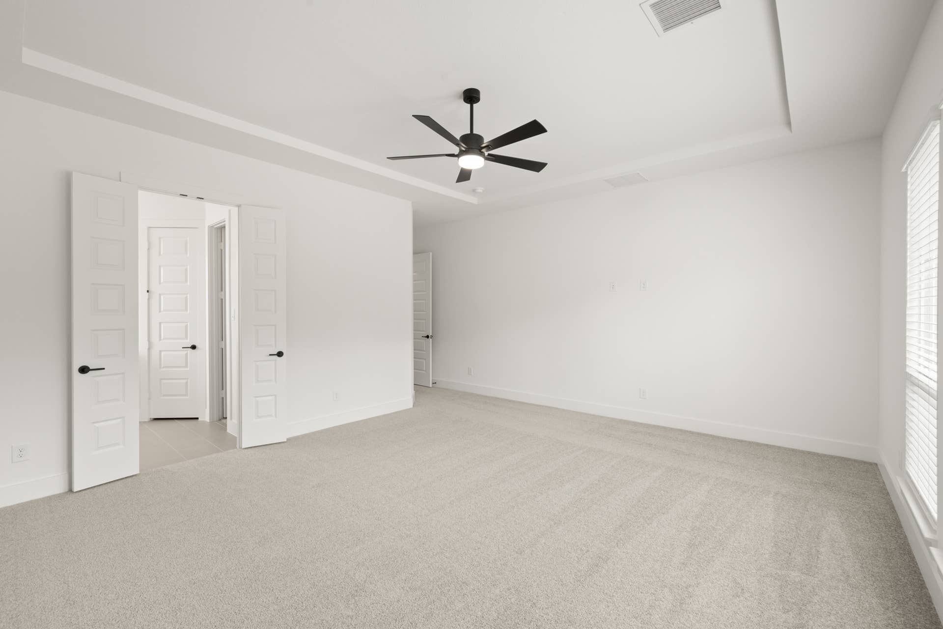 Spacious primary suite with tray ceiling and modern ceiling fan.