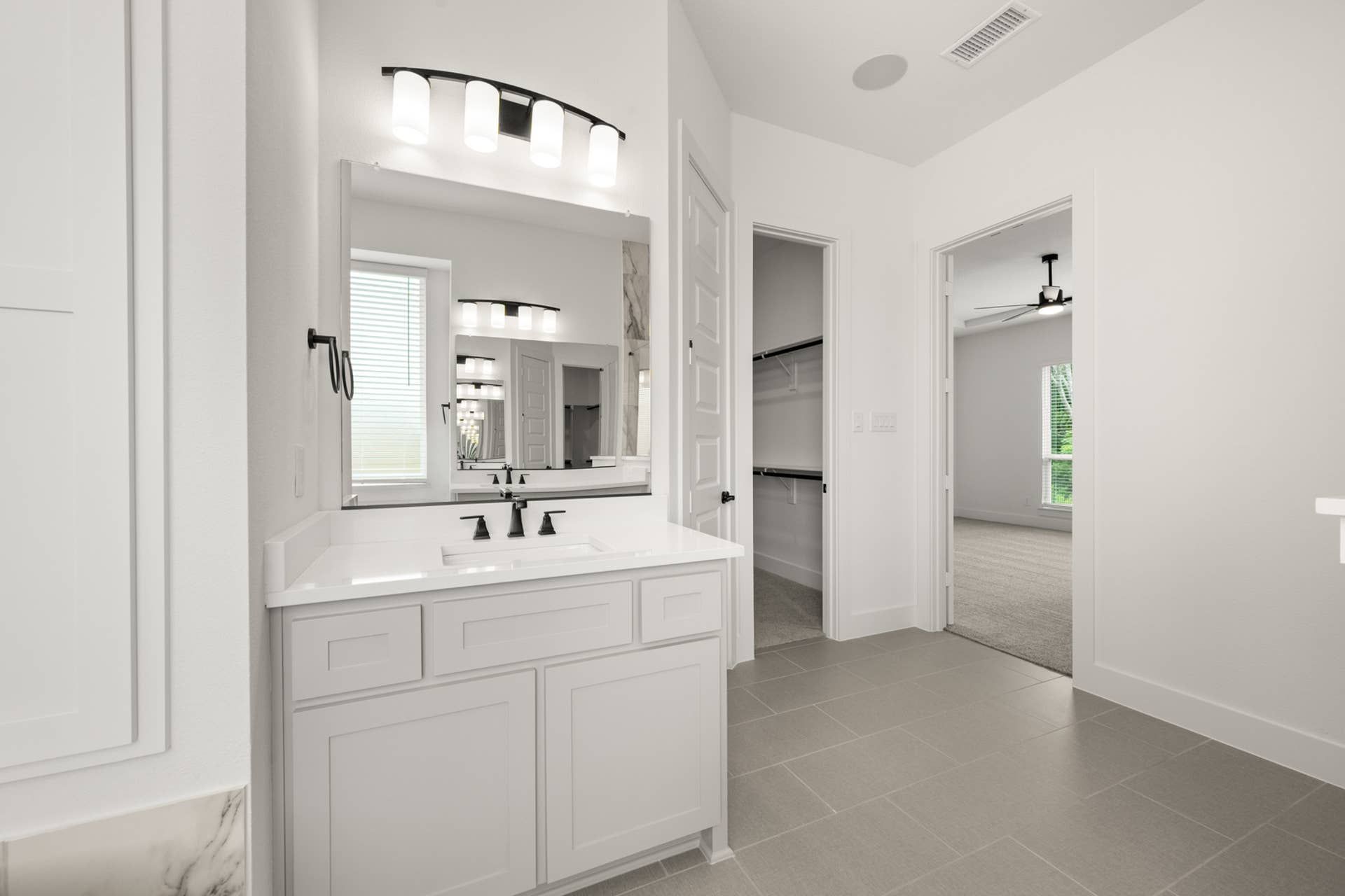 Modern bathroom with dual-sink vanity, elegant lighting, and walk-in closet access.
