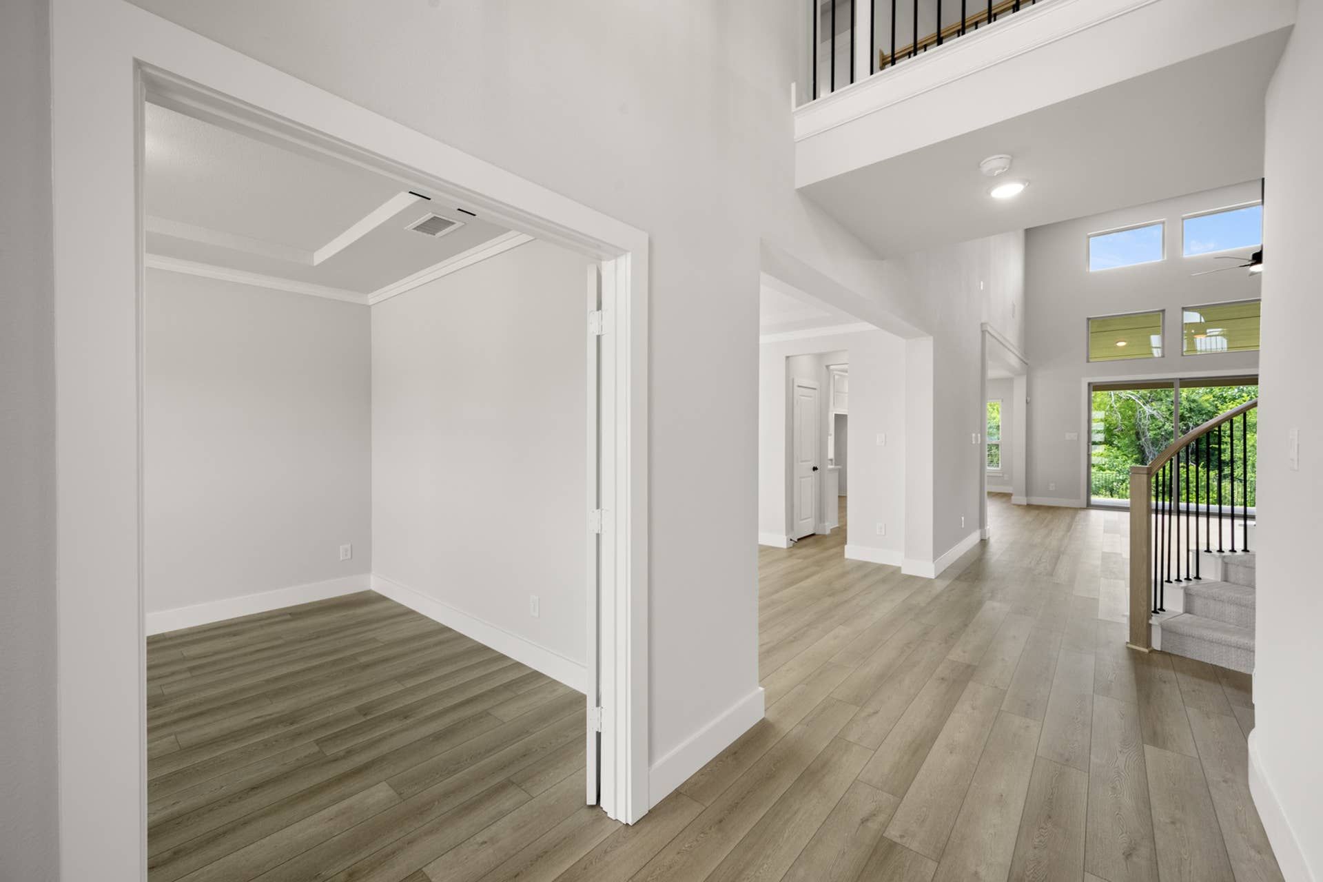 Spacious home entryway with wood flooring and large windows overlooking greenery.