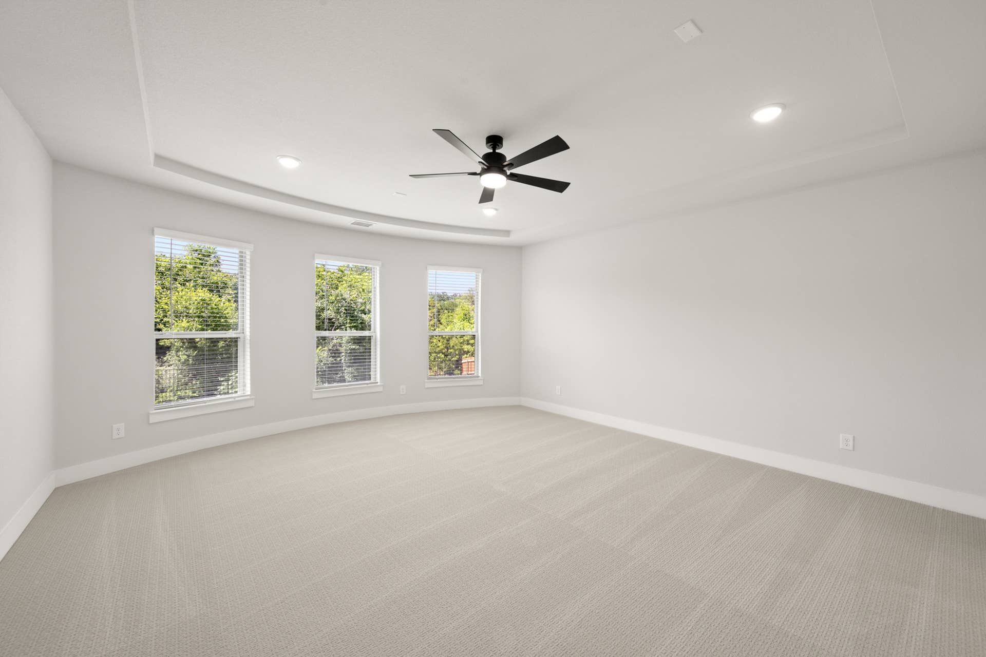Spacious primary suite with large windows and ceiling fan.