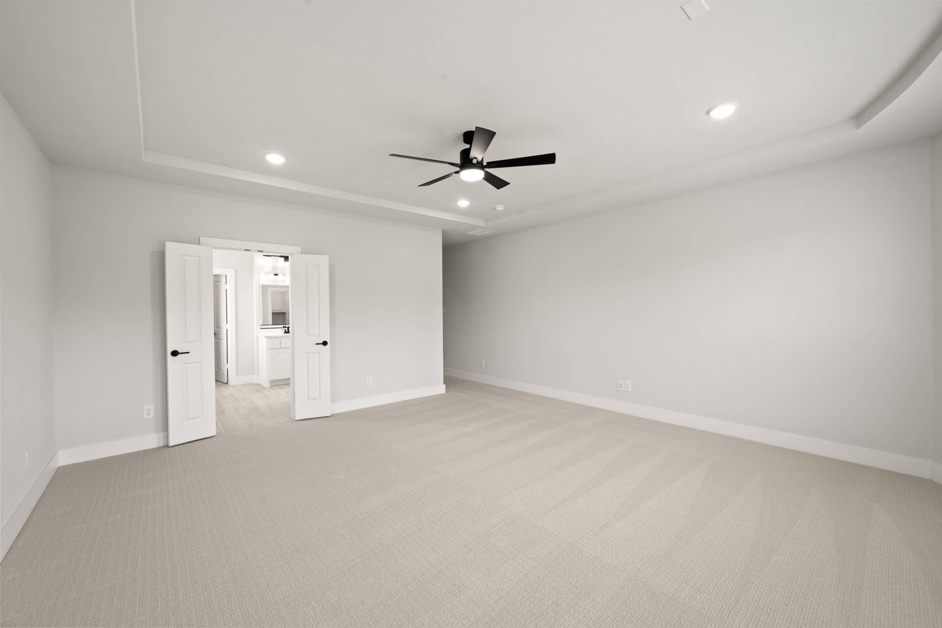 Spacious primary suite with neutral carpeting and modern ceiling fan.