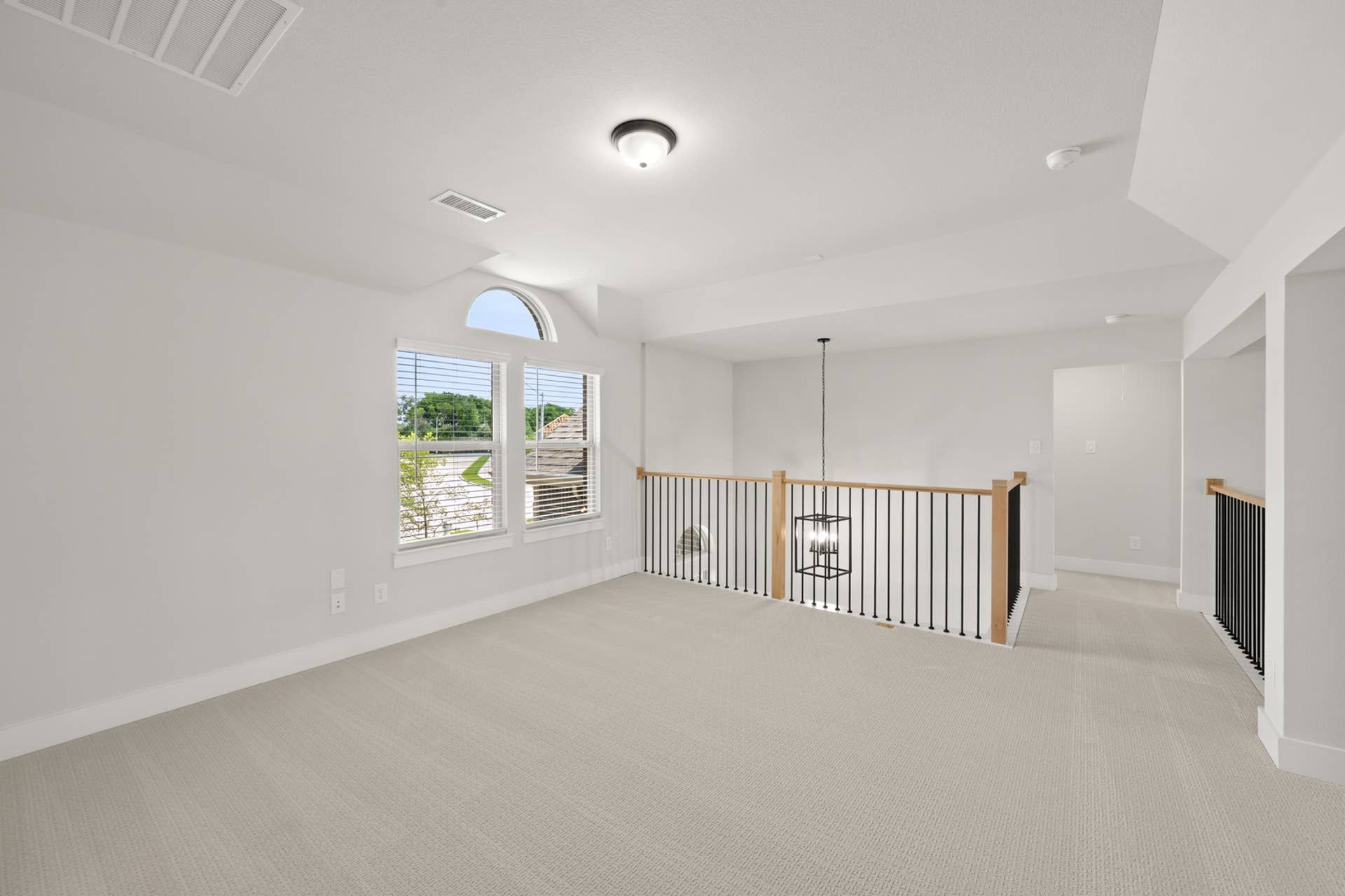 Spacious game room with carpeted floors and modern railing, featuring natural light.