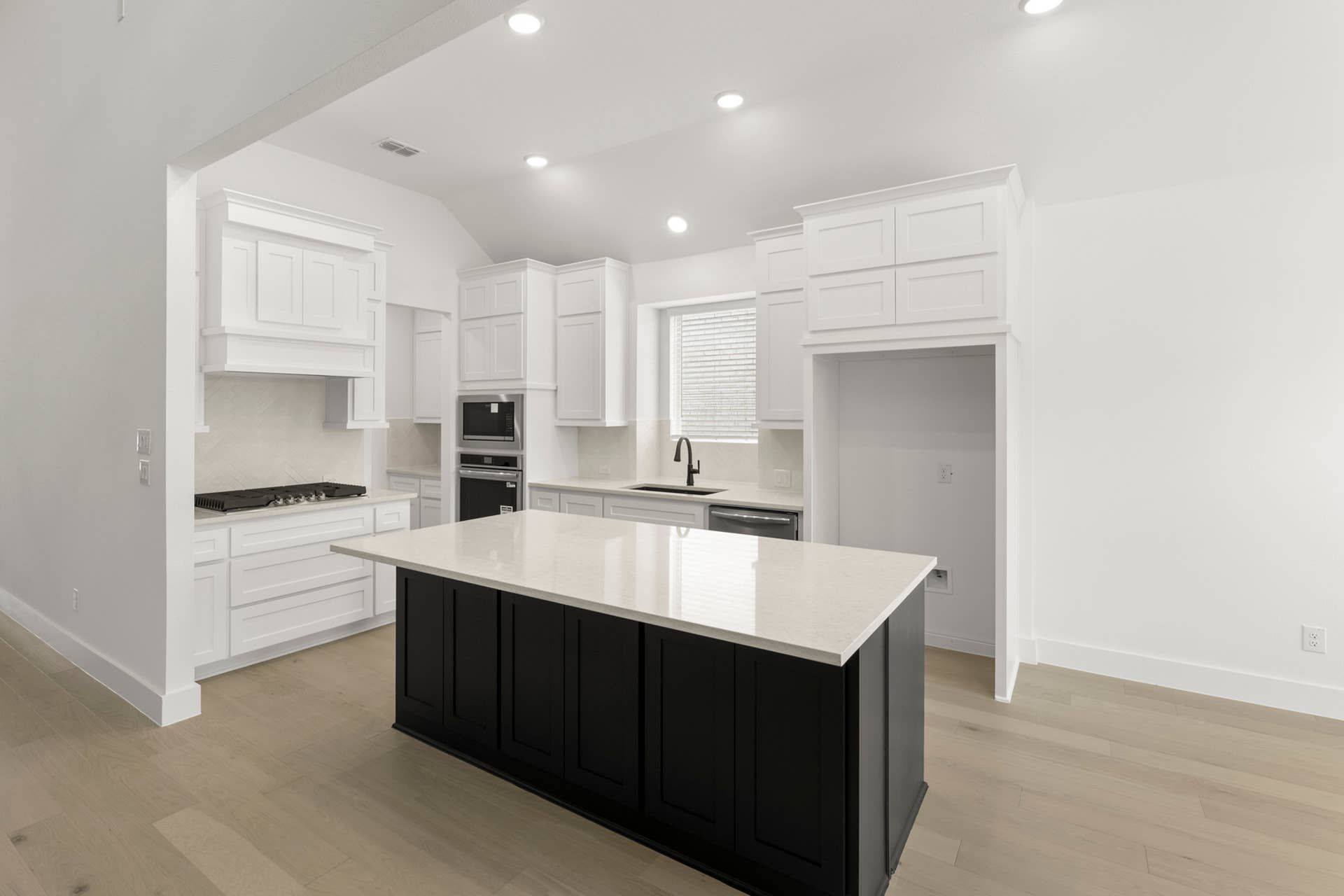 Modern kitchen with white cabinetry, black island, and recessed lighting.