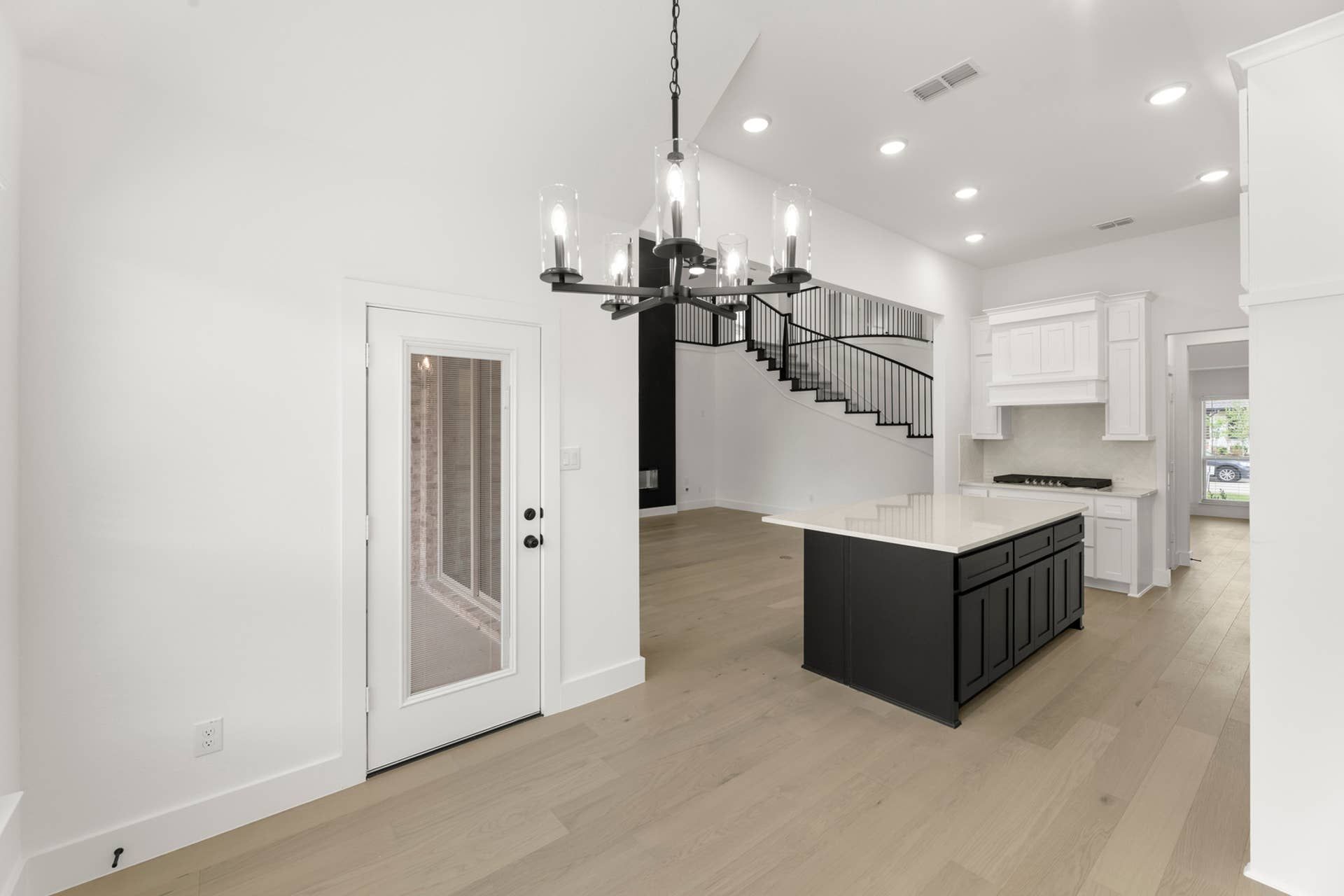 Modern kitchen interior with island, chandelier, and staircase view.
