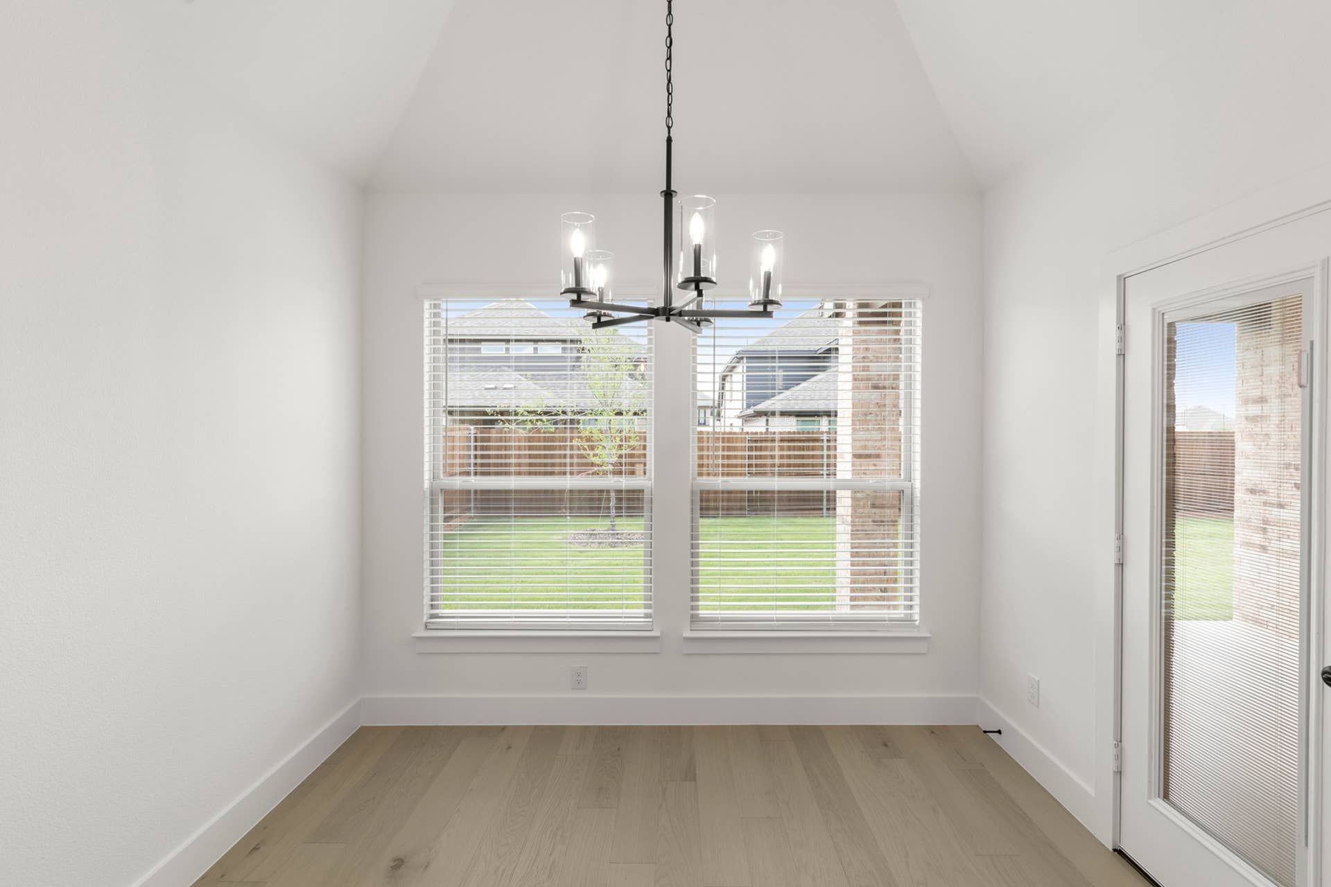 Bright dining nook with modern chandelier and large windows overlooking backyard.