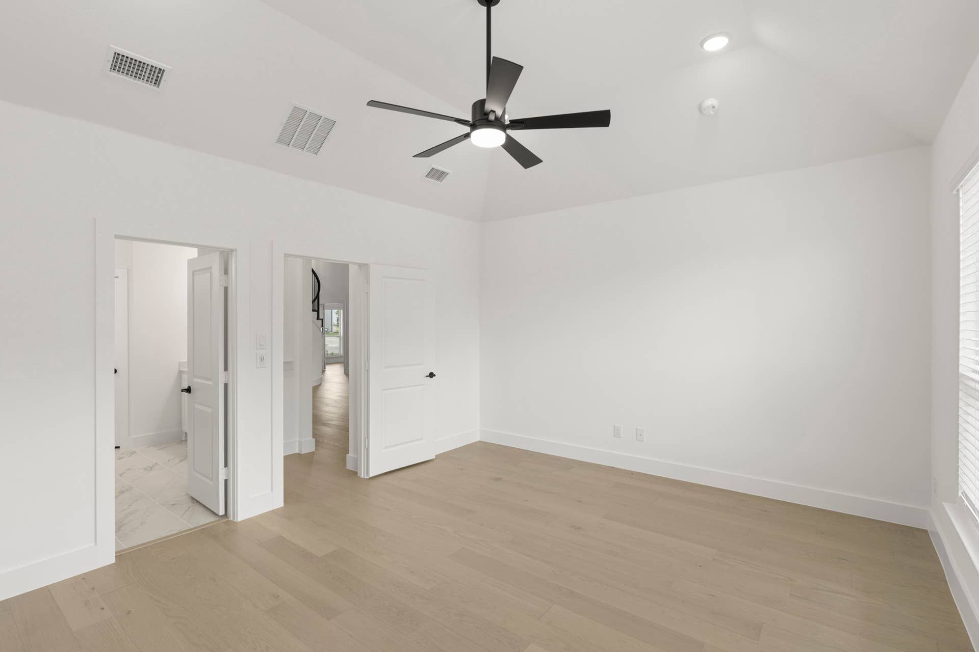 Spacious modern bedroom with light wood flooring and ceiling fan.