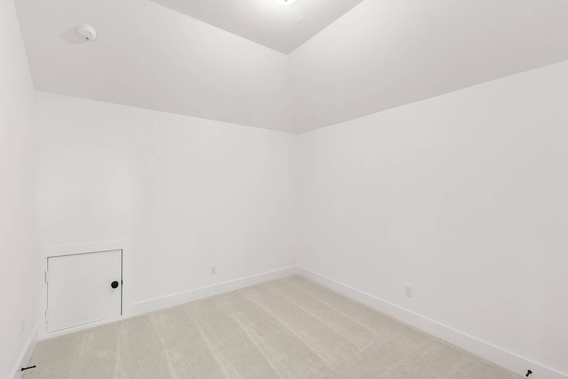 Minimalist room with sloped ceiling and small access door.