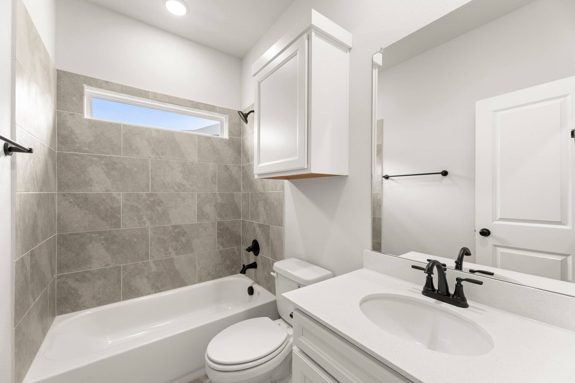 Modern bathroom with gray tile, white vanity, and black fixtures.