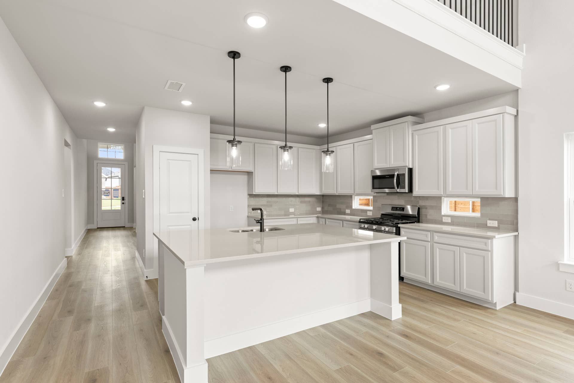 Modern kitchen with white cabinetry, pendant lights, and light wood flooring.