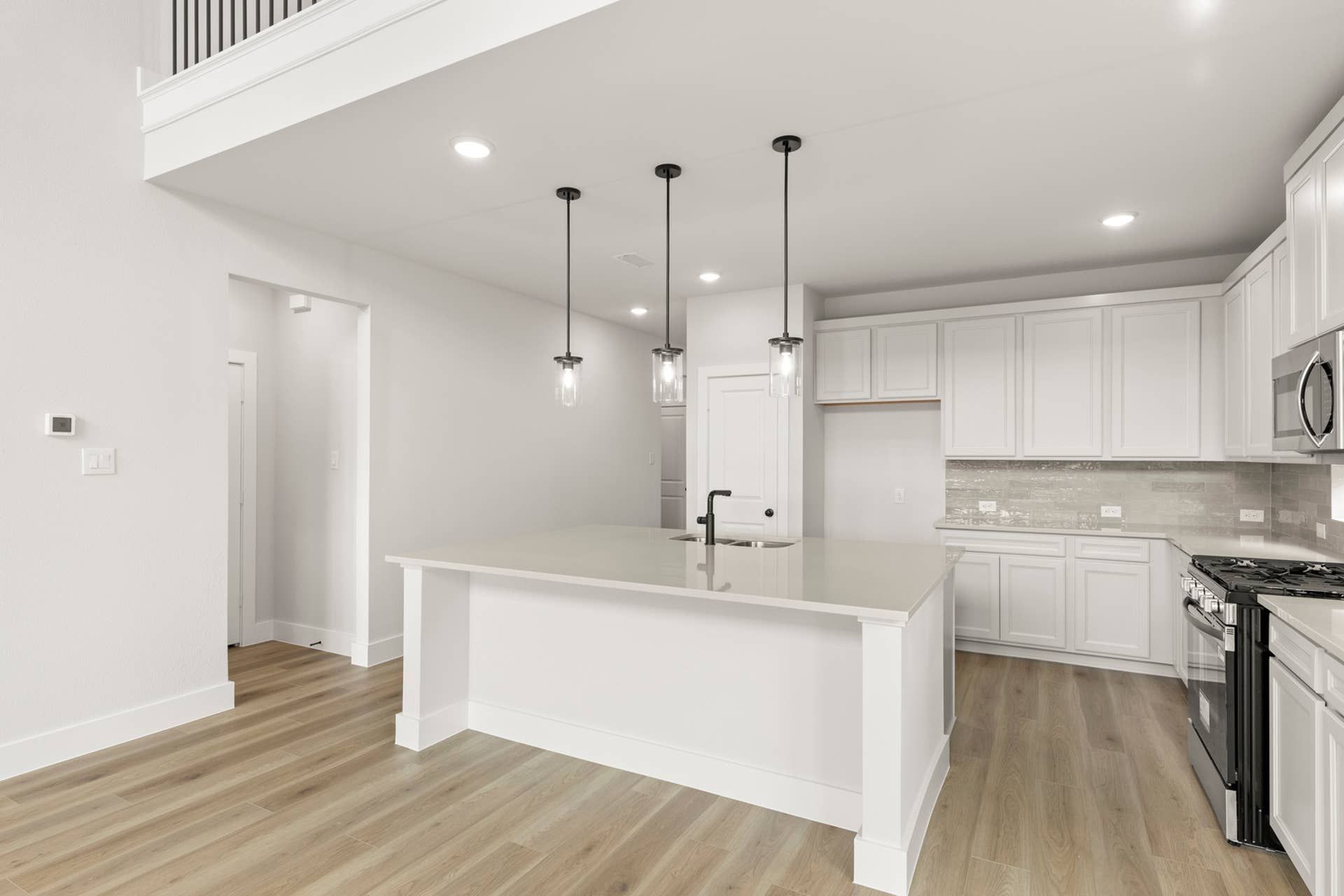 Modern kitchen with white cabinetry, pendant lighting, and hardwood floors.