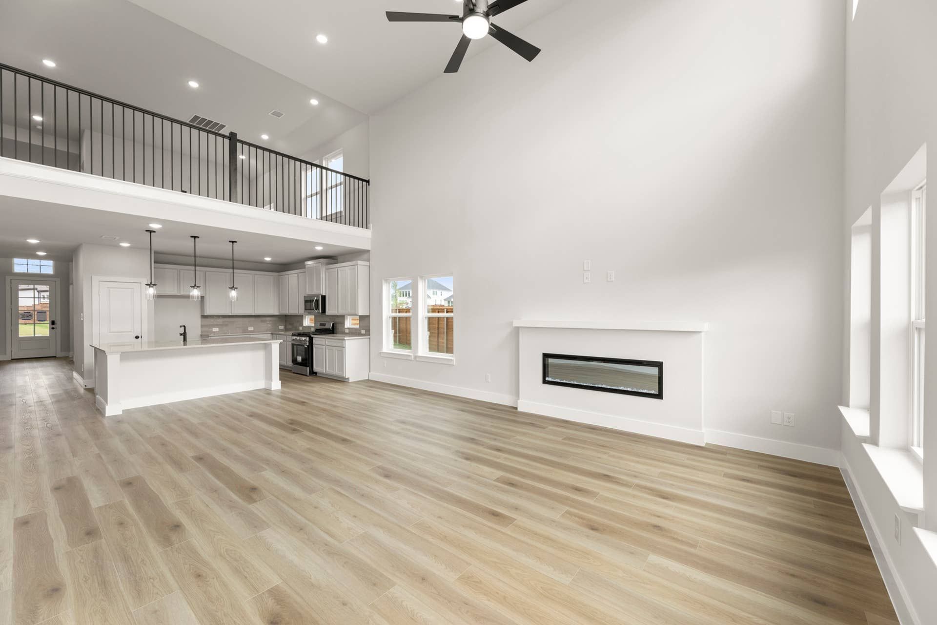Spacious modern family room with open kitchen, high ceilings, and wood flooring.