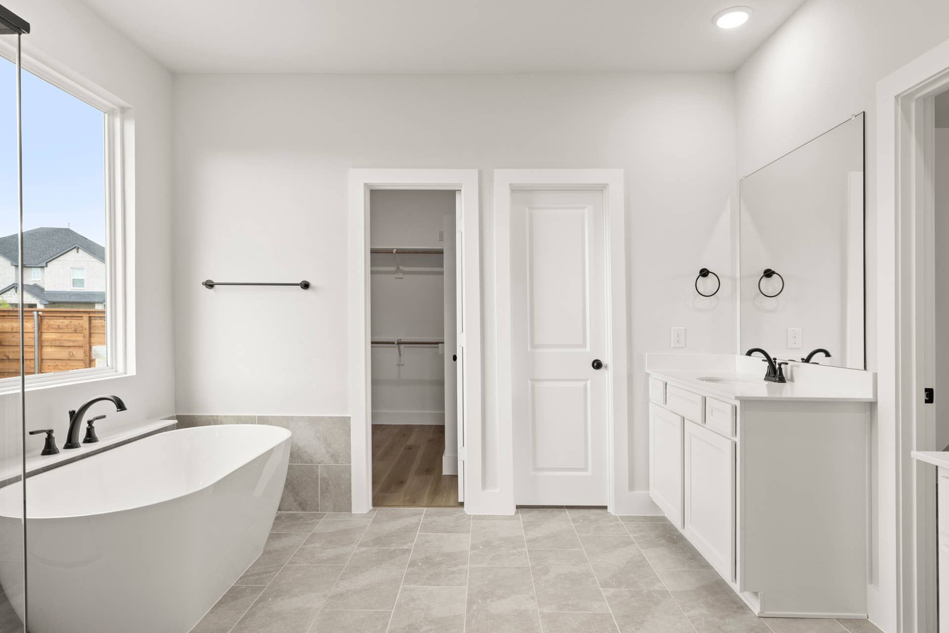 Modern bathroom with freestanding tub, large window, and walk-in closet.