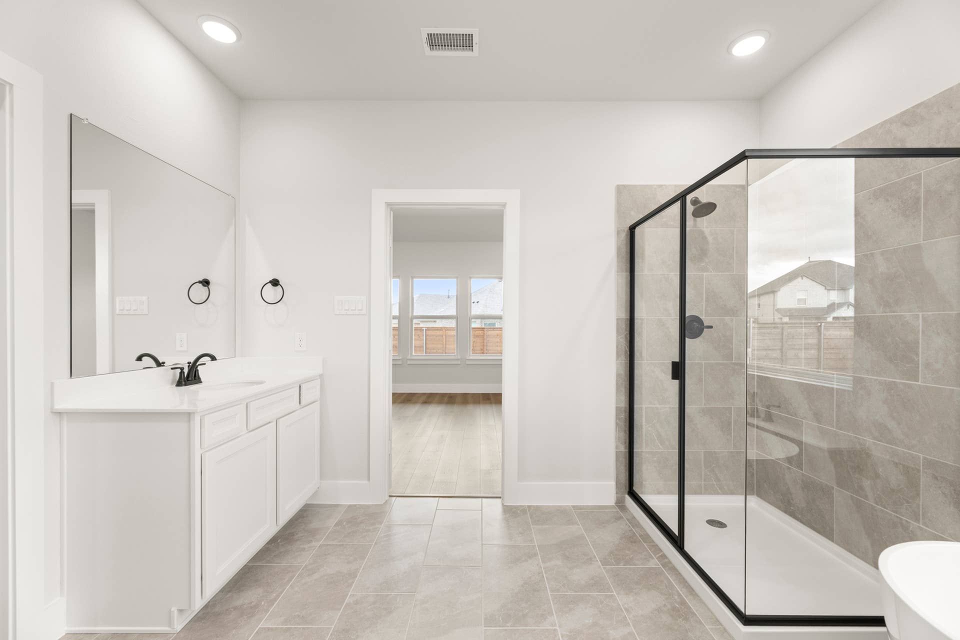 Modern bathroom with large mirror, dual sinks, and glass-enclosed shower.