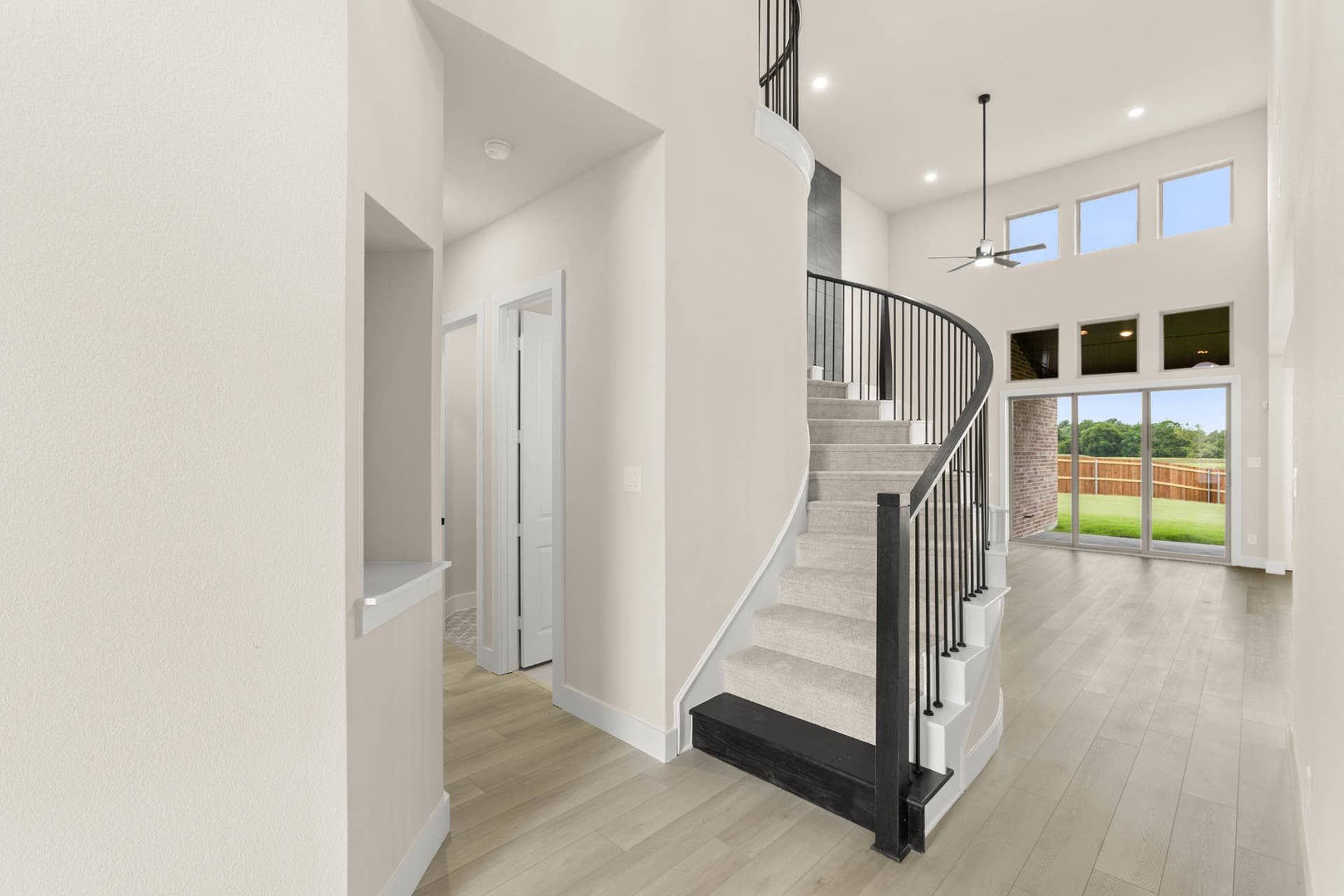 Spacious entryway with elegant spiral staircase and large windows overlooking backyard.