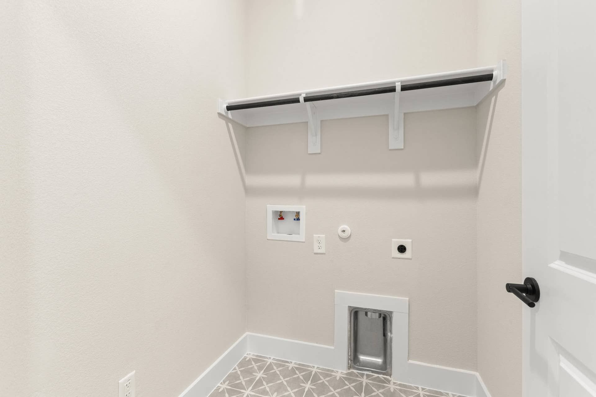 Utility room with wall shelf, plumbing, and electrical hookups.